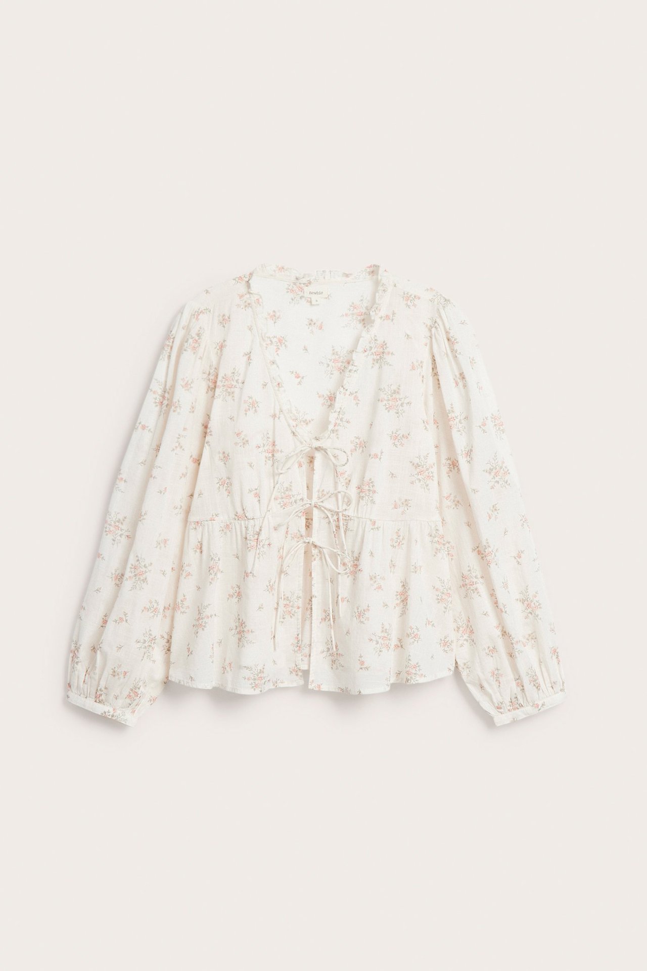 Frontvisning: En kremhvit bomullsbluse med blomstermønster, peplumkant og V-hals med knyting foran.