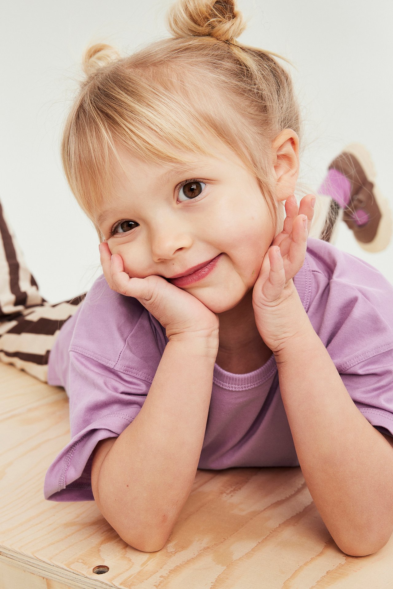 Zbliżenie na uśmiechnięte dziecko w jasnofioletowej bawełnianej koszulce i spodniach w paski.
