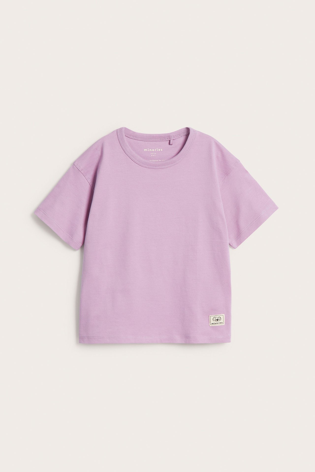 Widok z przodu: jednokolorowy liliowy bawełniany T-shirt dziecięcy z prążkowanym okrągłym dekoltem i tkaną naszywką.