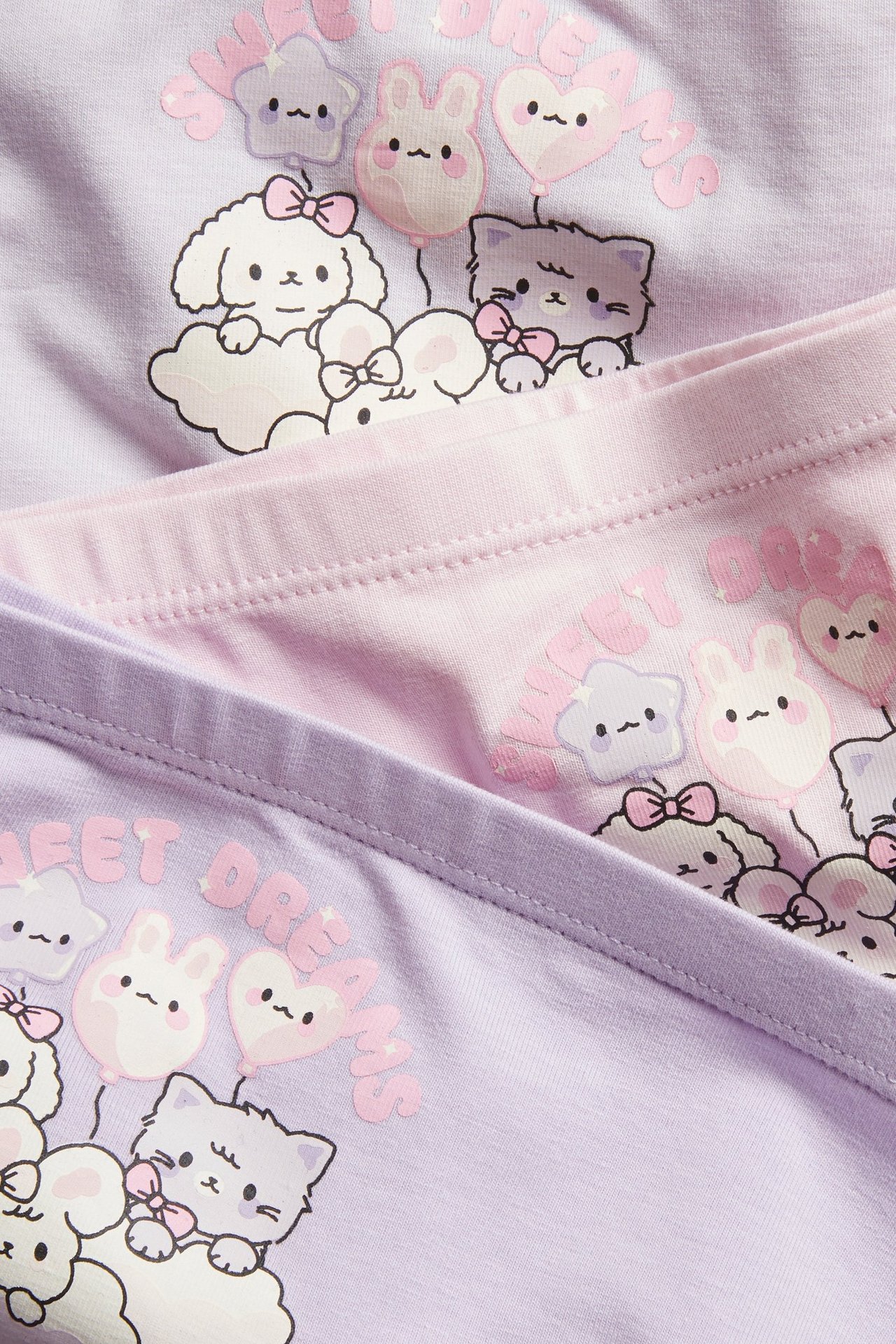 Zbliżenie na trzy pary wzorzystych bokserek dziecięcych w jasnym liliowym i jasnym różowym kolorze z uroczymi nadrukami.