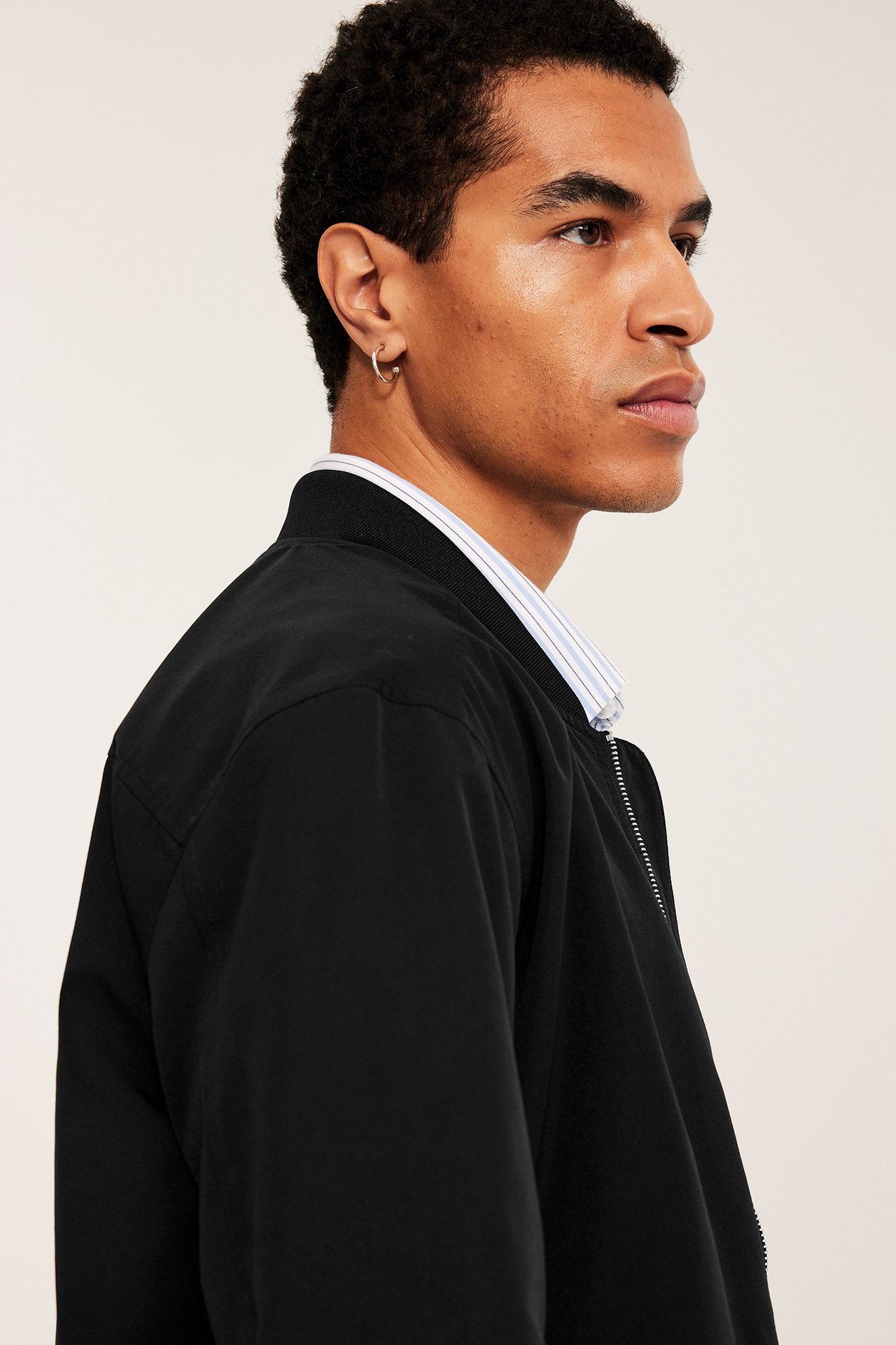 Sidebilde av en mann i svart bomberjakke over stripete skjorte, med gullring i øret.