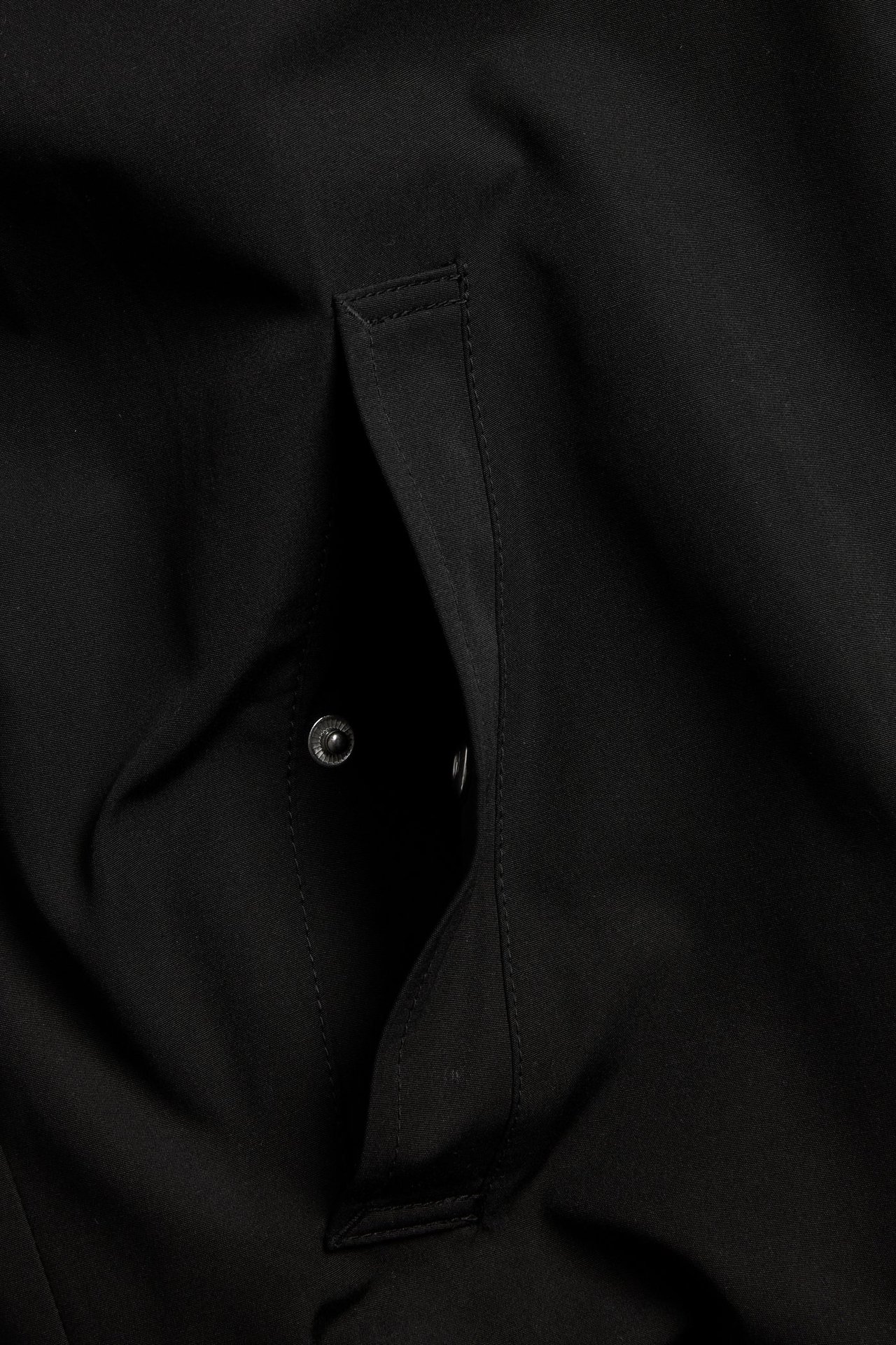 Zbliżenie na przednią kieszeń czarnej kurtki bomberki z zapięciem na zatrzask.