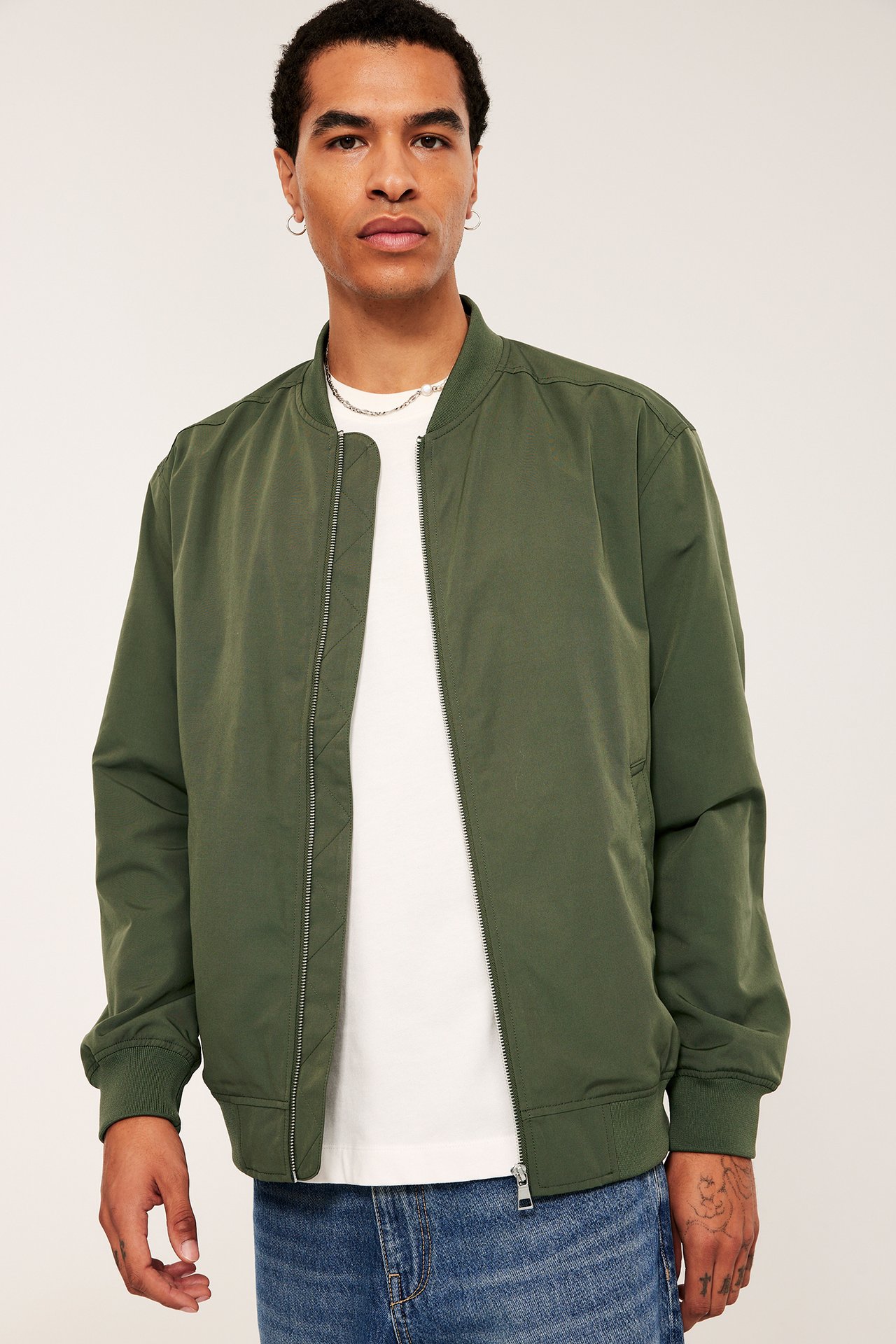 Forfra: Mann i åpen mørkegrønn bomberjakke over en hvit t-skjorte og blå jeans.