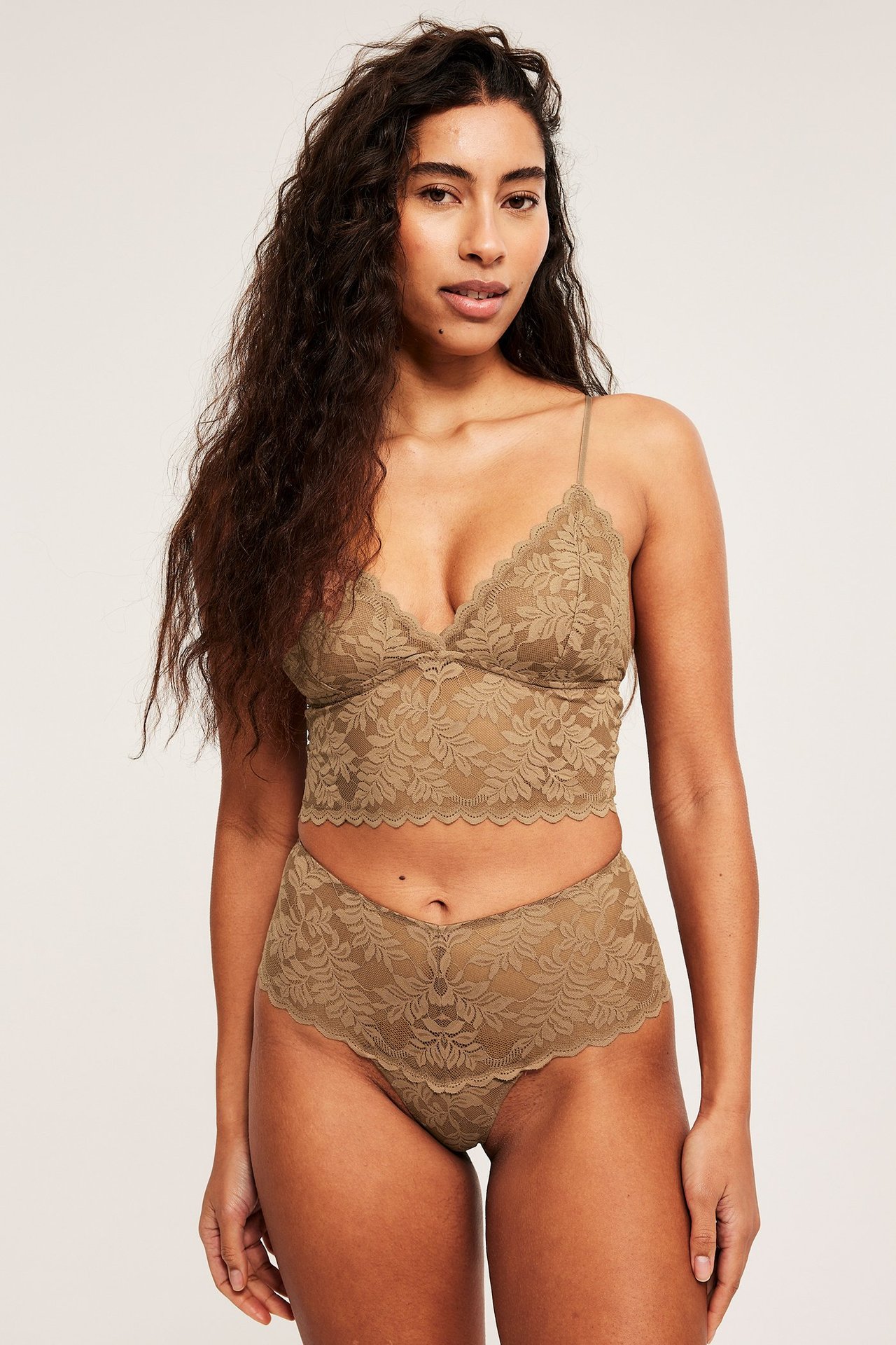 Widok z przodu kobiety w brązowym koronkowym biustonoszu typu longline na cienkich ramiączkach i pasujących koronkowych majtkach.