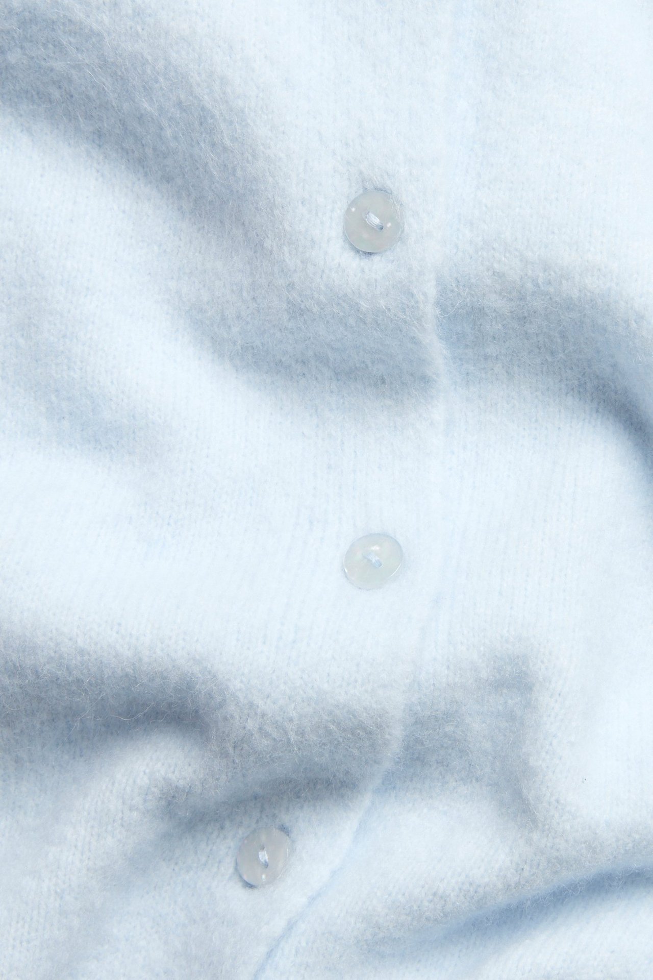 Zbliżenie jasnoniebieskiego cienkiego kardiganu z trzema widocznymi perłowymi guzikami.