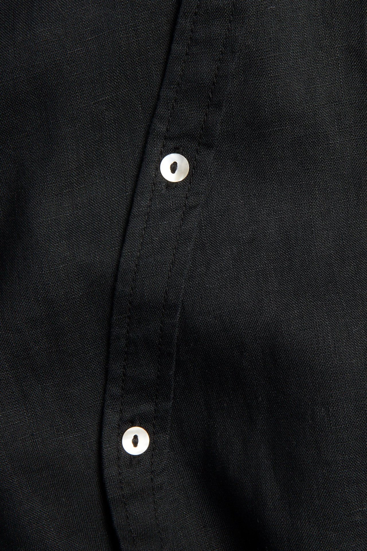 Lähikuva mustasta pellavapuserosta, jossa valkoiset napit vinossa nappilistassa.