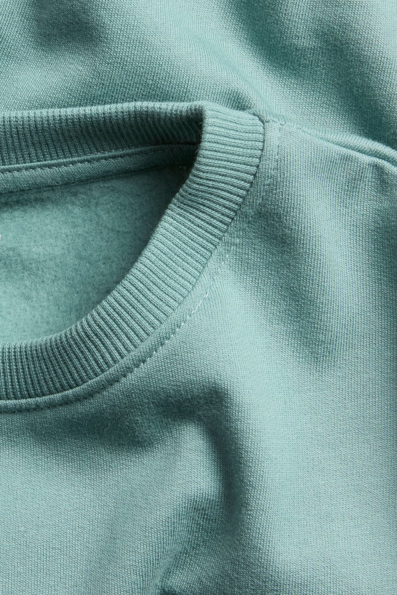 Nærbilde av en lysegrønn sweatshirt i bomull med ribbet hals og myk innside.