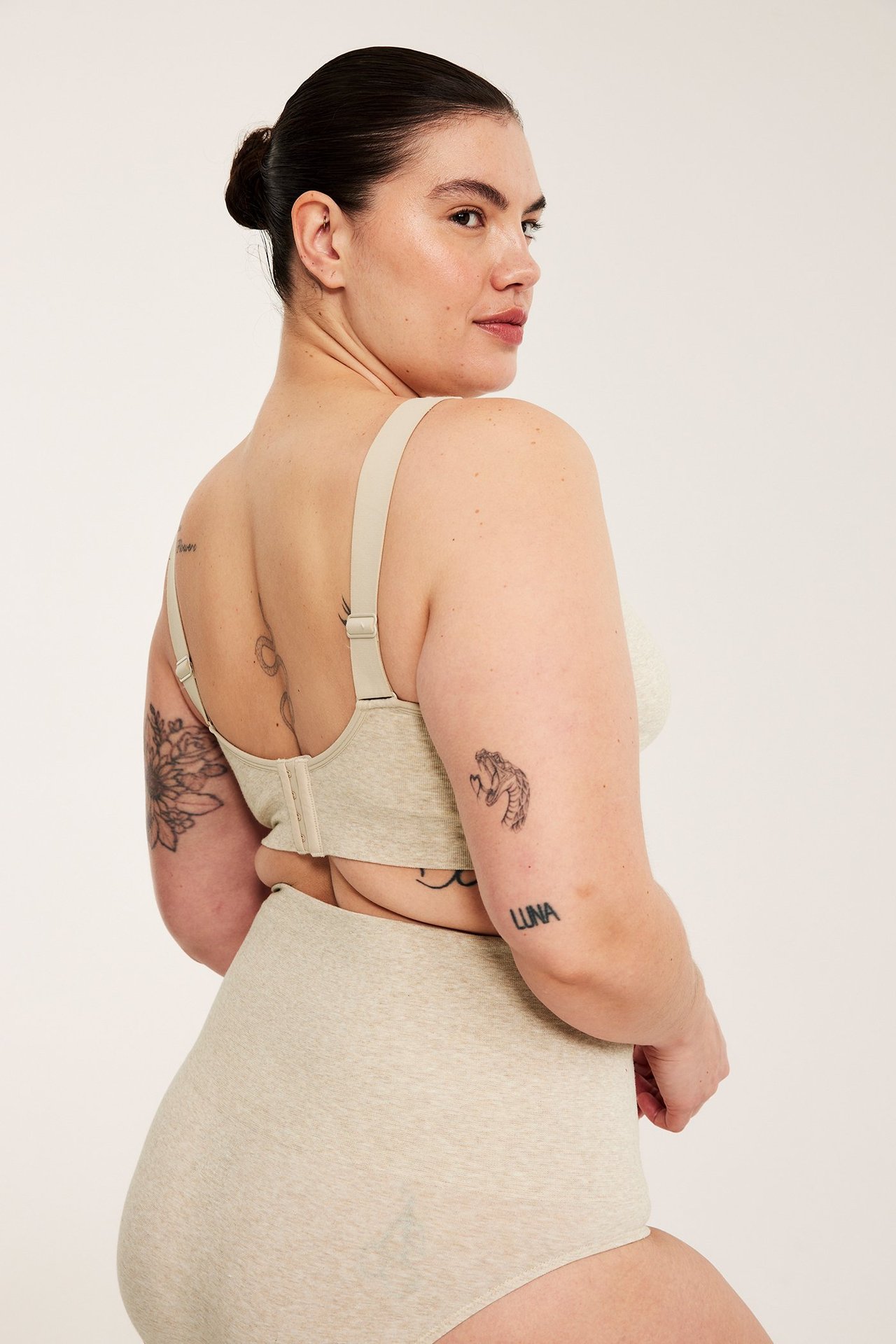 Side-bakfra visning av kvinne i beige melert sømløs BH og matchende høy midje-truser.