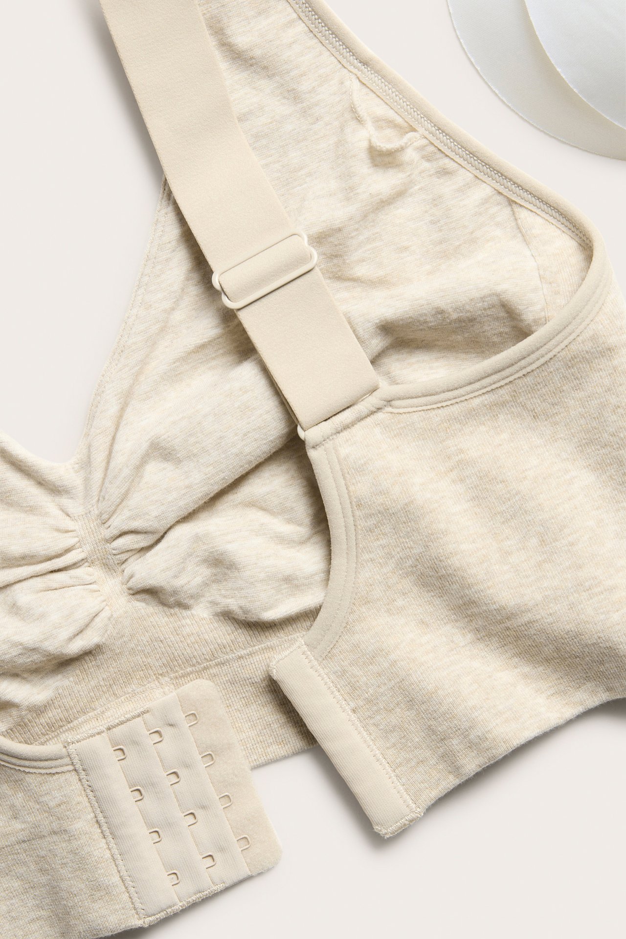 Nærbilde av beige melert sømløs BH med brede justerbare stropper og fire-rads hekte-og-malje-lukking.