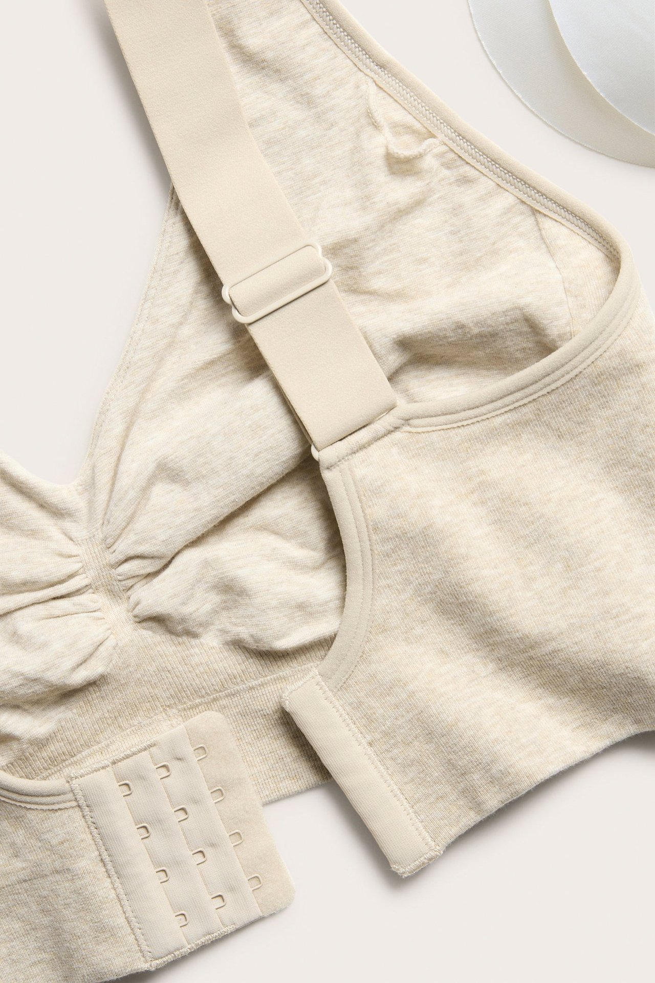 Nærbilde av beige melert sømløs BH med brede justerbare stropper og fire-rads hekte-og-malje-lukking.