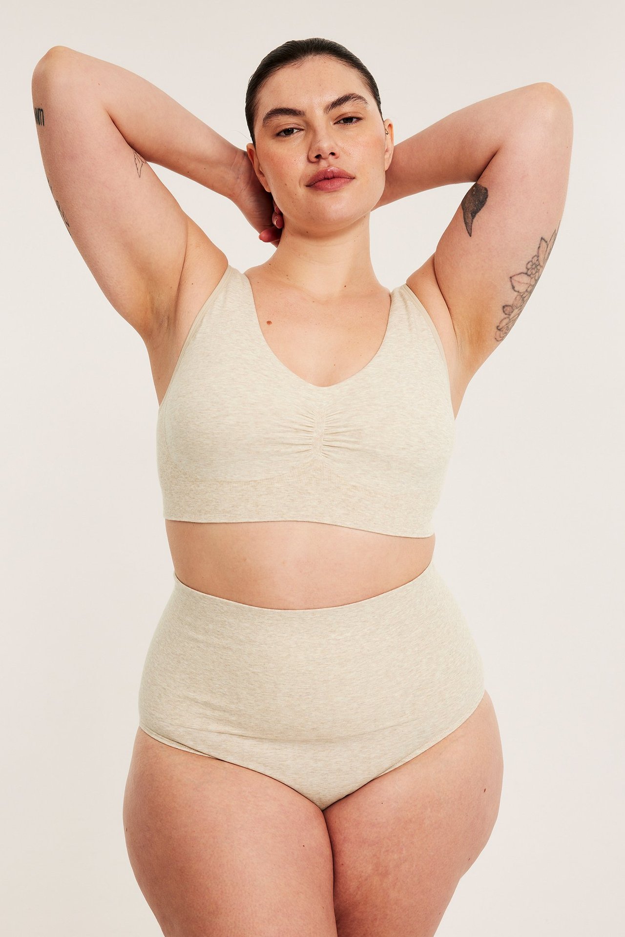 Frontbilde av en kvinne i en beige melert sømløs BH med rynket front og matchende høy truse.