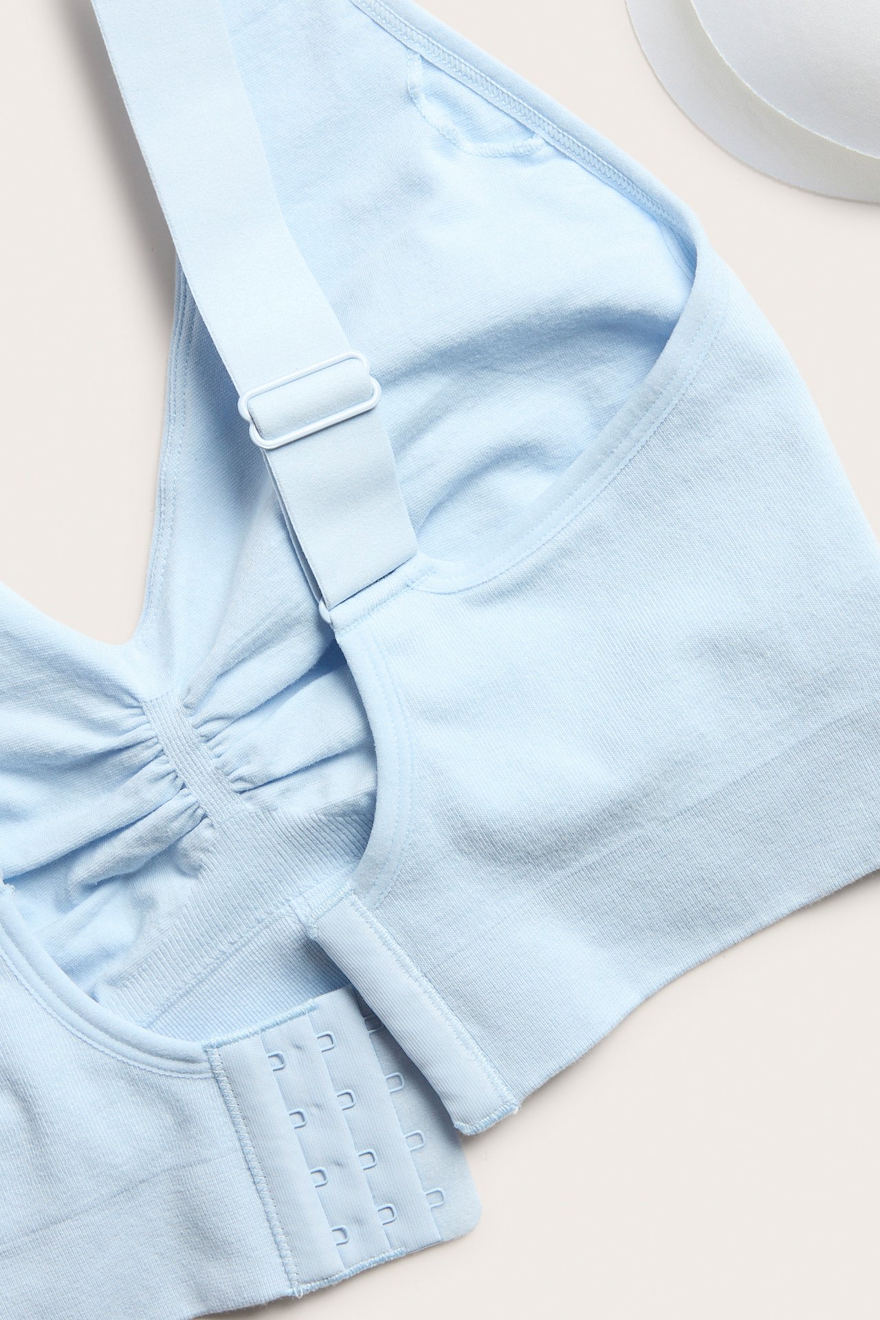 Nærbilde av en lyseblå sømløs BH i bomullsblanding med brede stropper og knapperad med fire hekter.