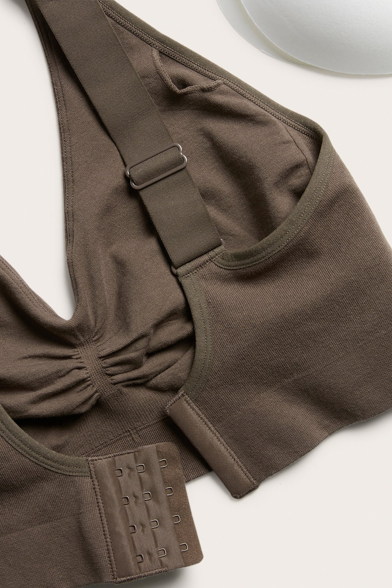 Nærbilde: mørkebrun sømløs bomulls-BH med brede stropper, hektefeste bak, og uttakbar polstring.