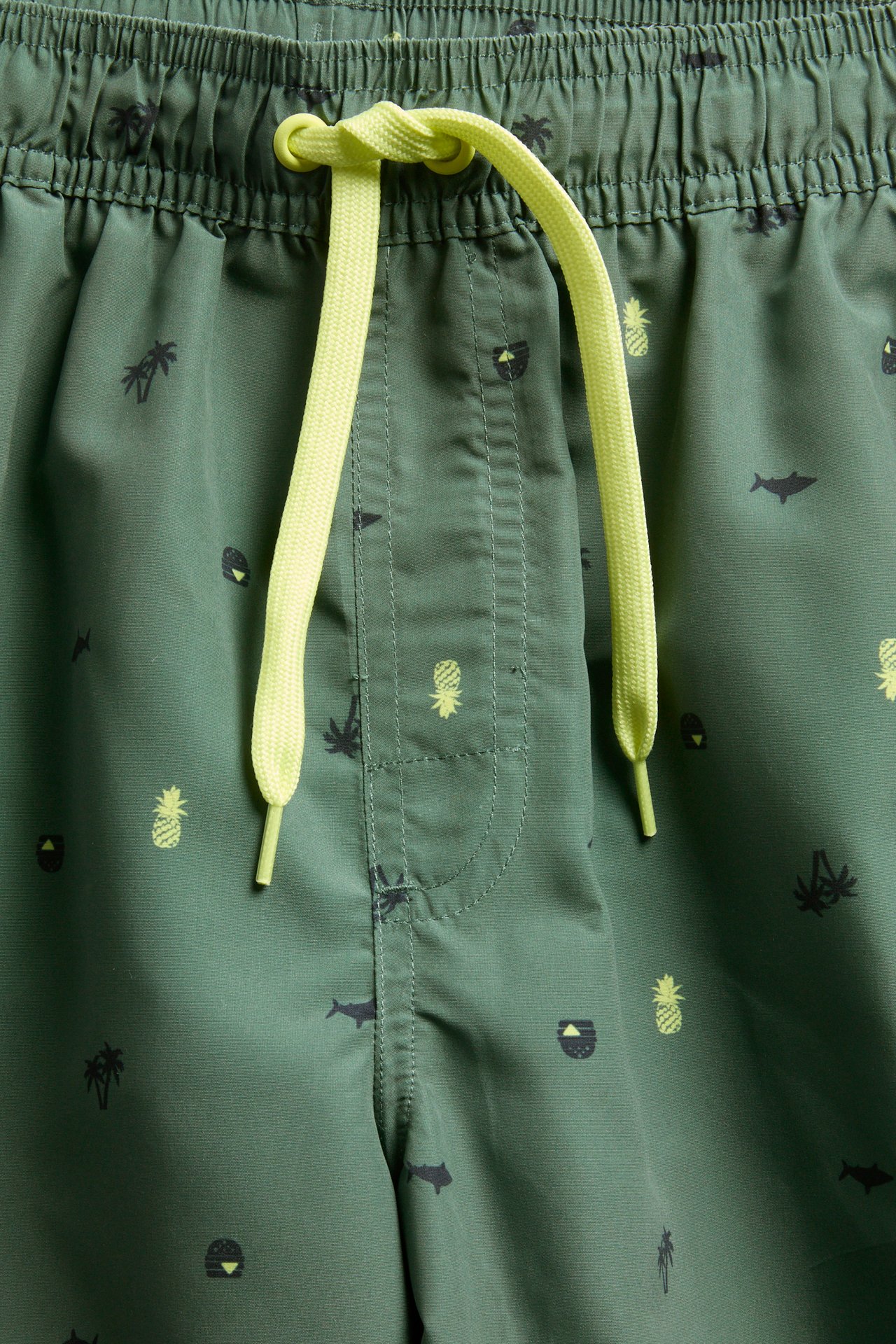 Nærbilde av grønne mønstrede badeshorts med elastisk linning og neongule snøringer.