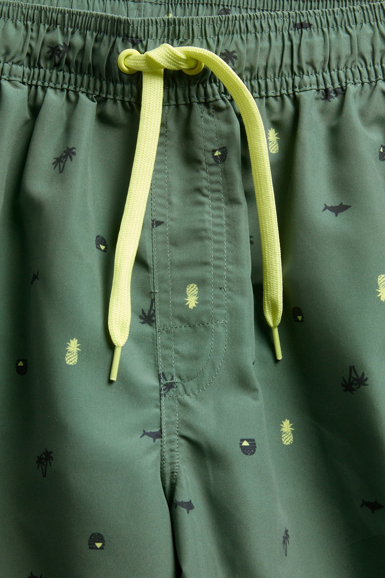 Zbliżenie zielonych, wzorzystych szortów kąpielowych z elastycznym pasem i neonowo żółtymi sznurkami.