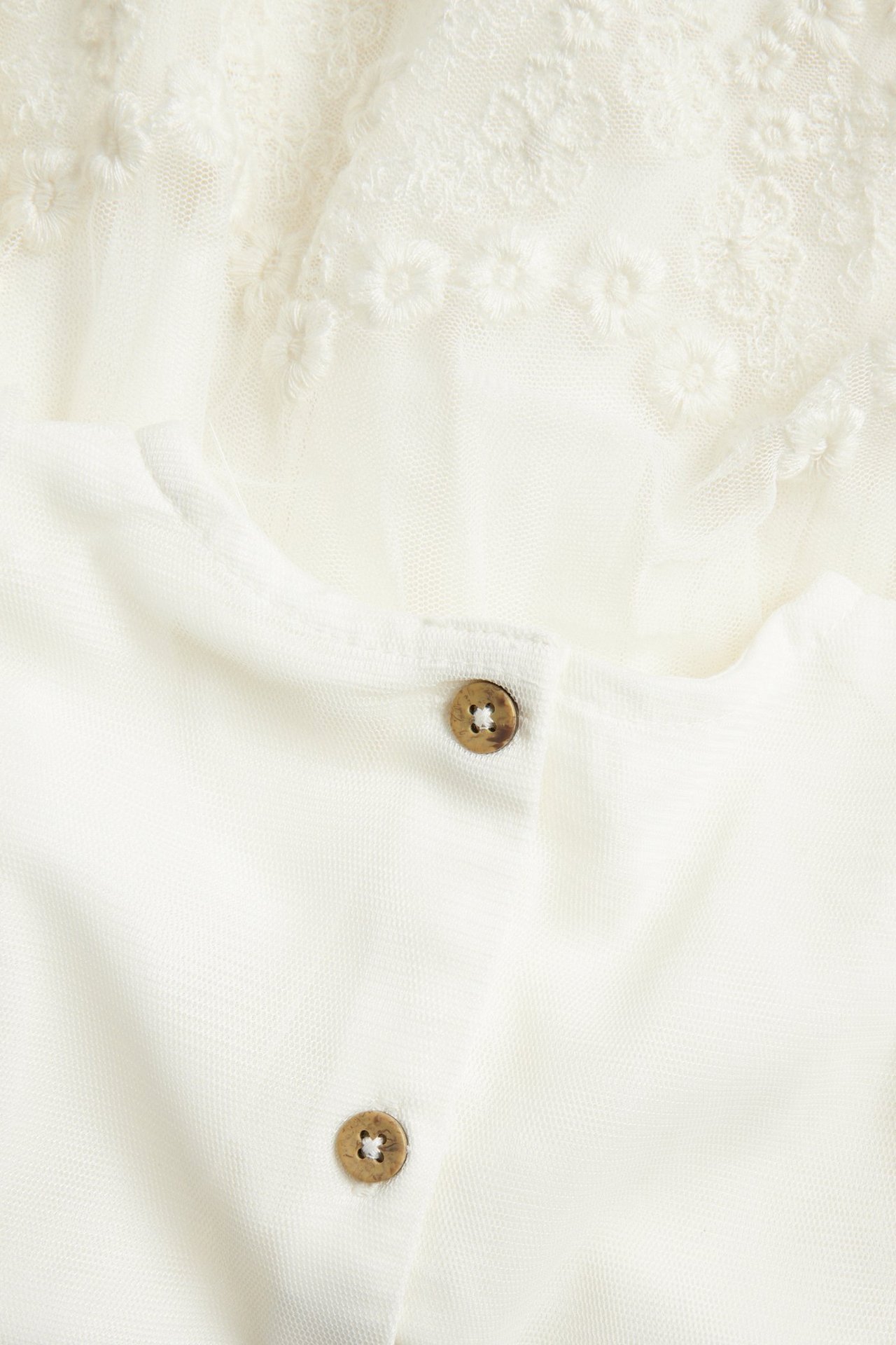 Zbliżenie z tyłu na sukienkę z kremowej siateczki z haftem i dwoma małymi drewnianymi guzikami.