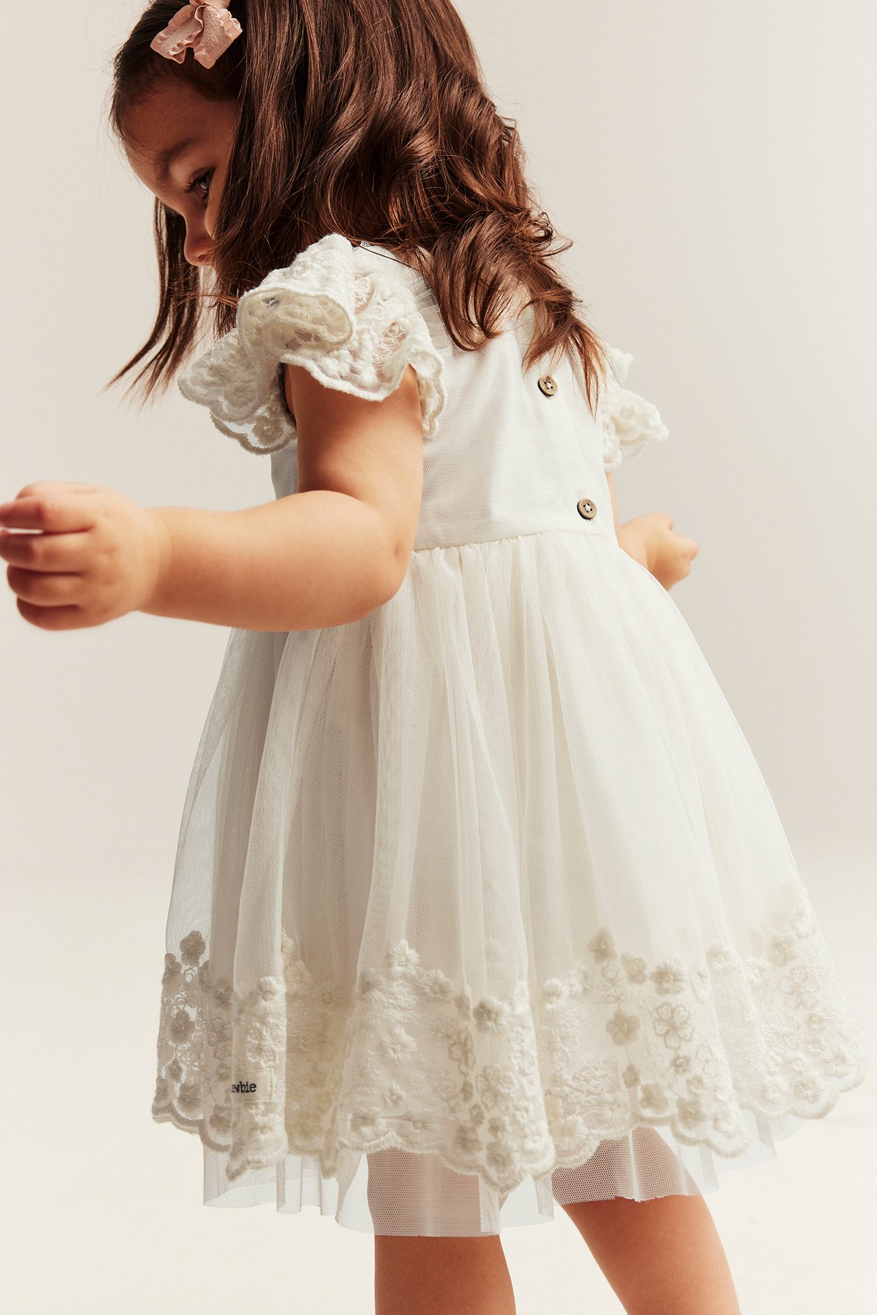 Lapsi luonnonvalkoisessa brodeeratussa verkkomekossa, röyhelöhihat ja takana napit, sivu-takaa.