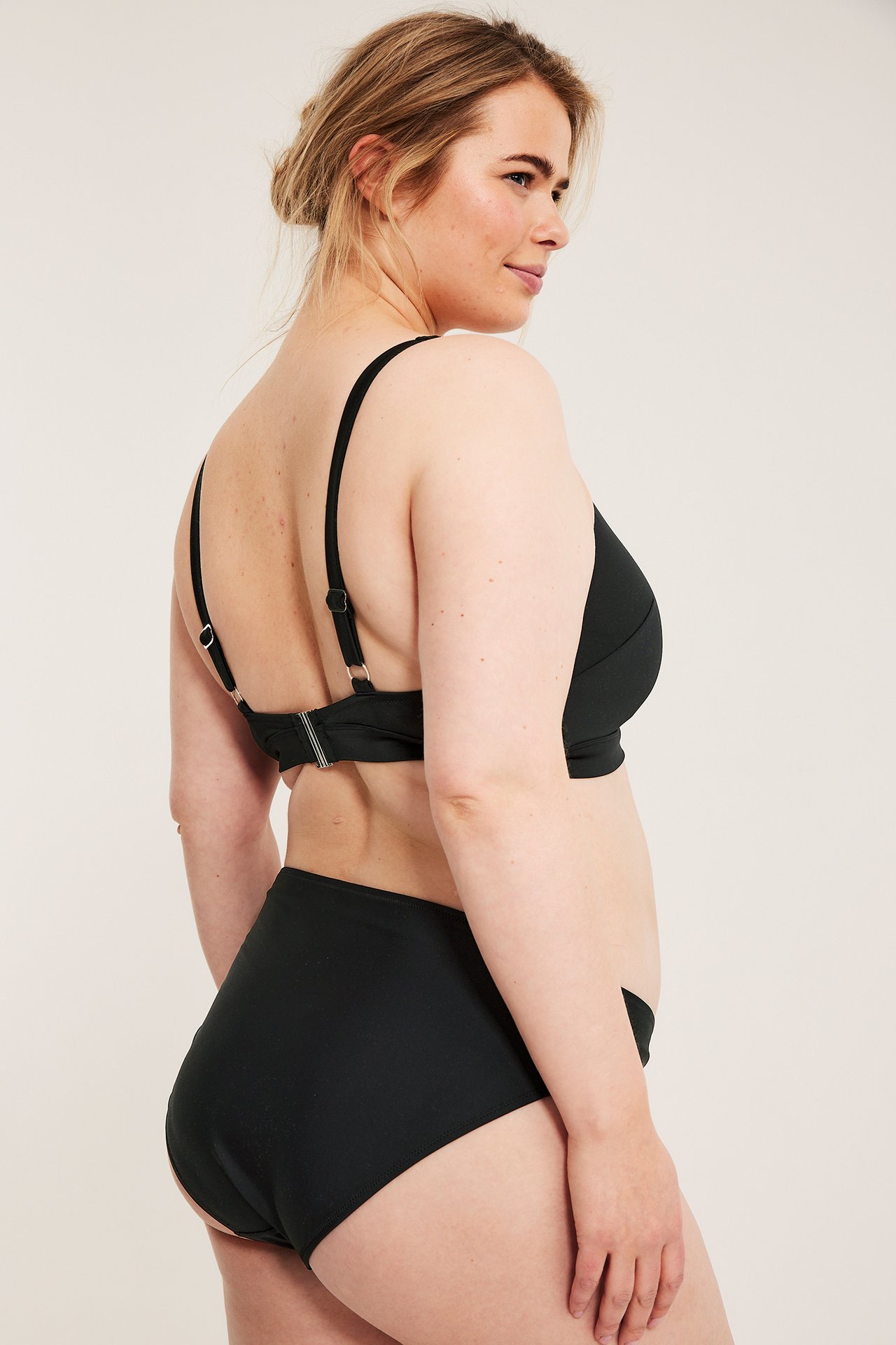 Sidevisning av en kvinne i svart ensfarget bikinitruse og matchende svart bikinitopp.