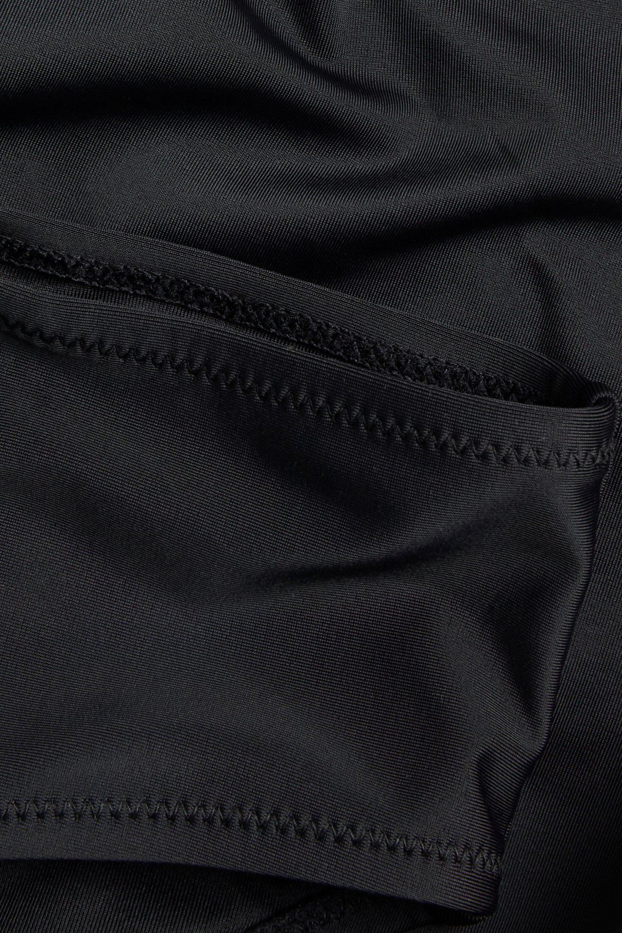 Lähikuva yksivärisestä mustasta bikinialaosasta, joka näyttää kankaan ja siksak-ompelun.