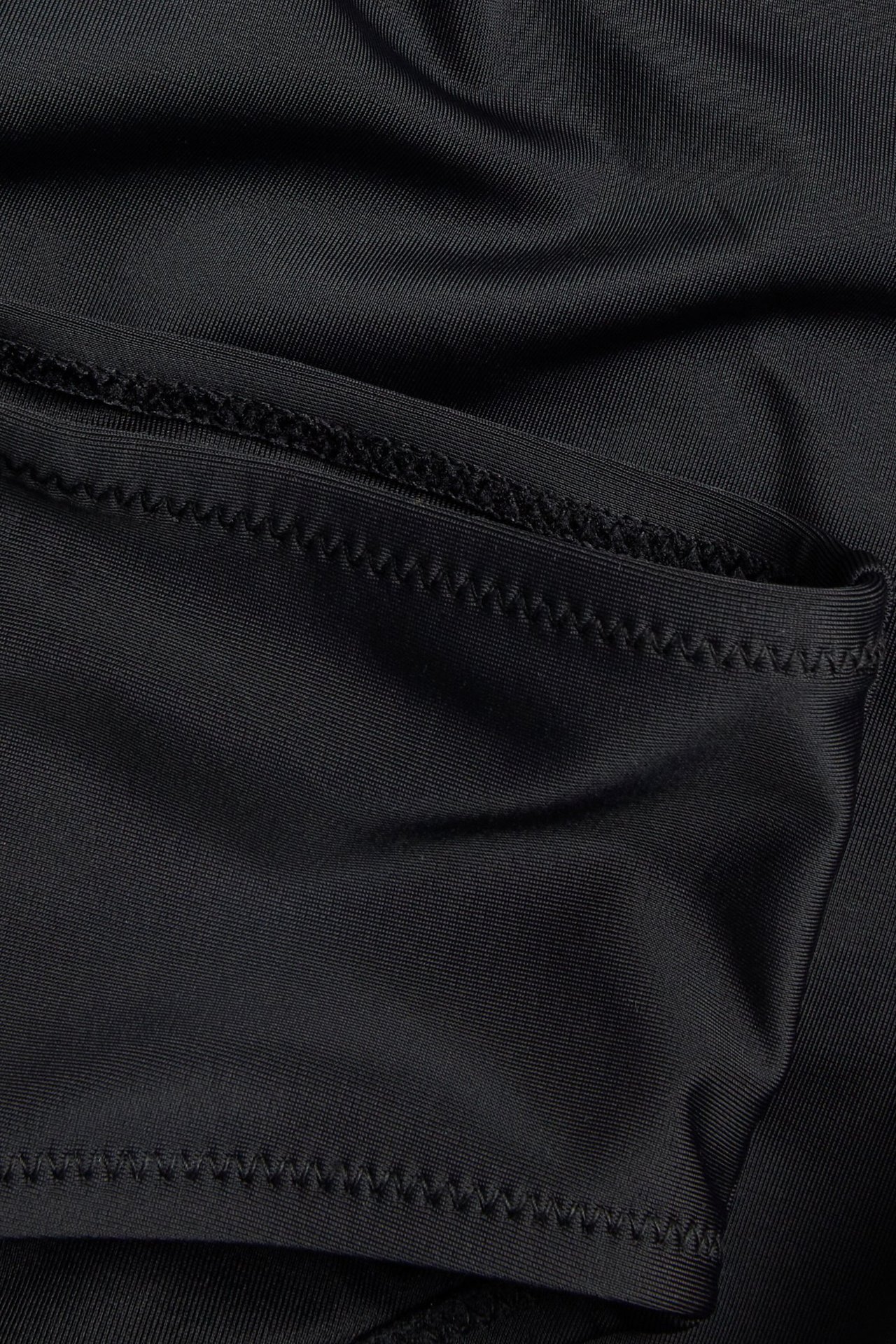 Lähikuva yksivärisestä mustasta bikinialaosasta, joka näyttää kankaan ja siksak-ompelun.