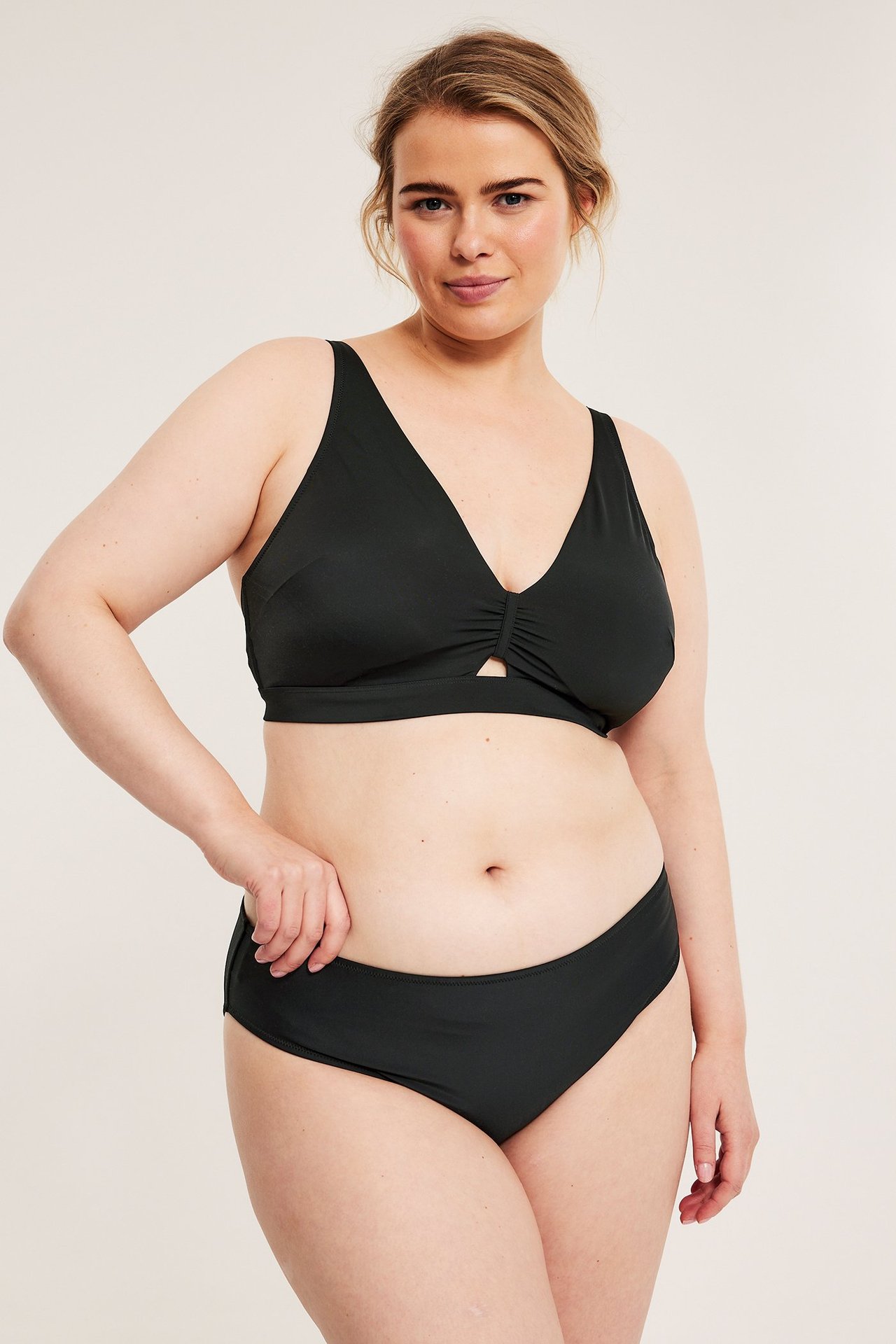 Forfra: kvinne i svart ensfarget bikiniunderdel og matchende svart rynket bikinitopp.