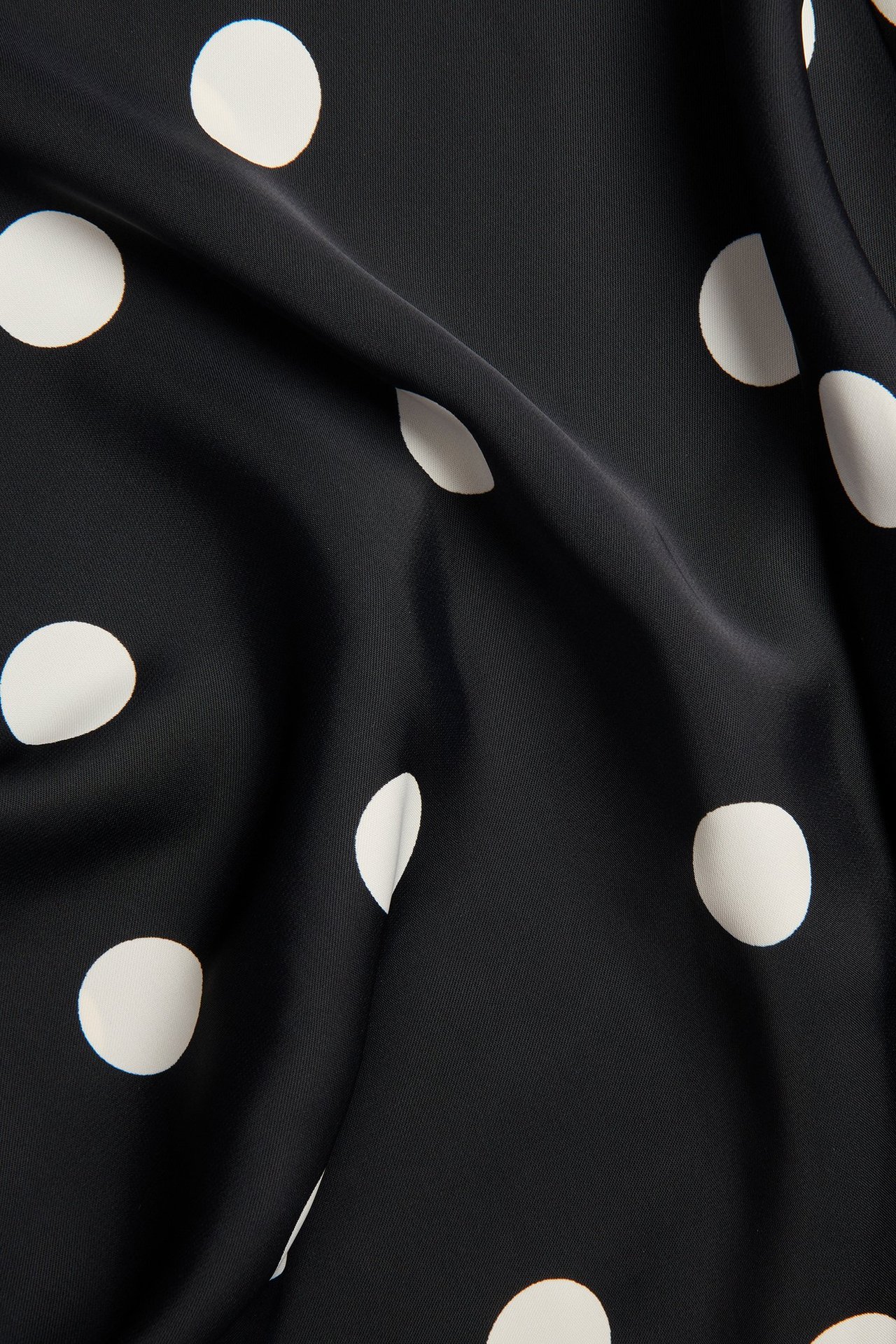 Zbliżenie na czarną, błyszczącą spódnicę z poliestru w białe kropki.
