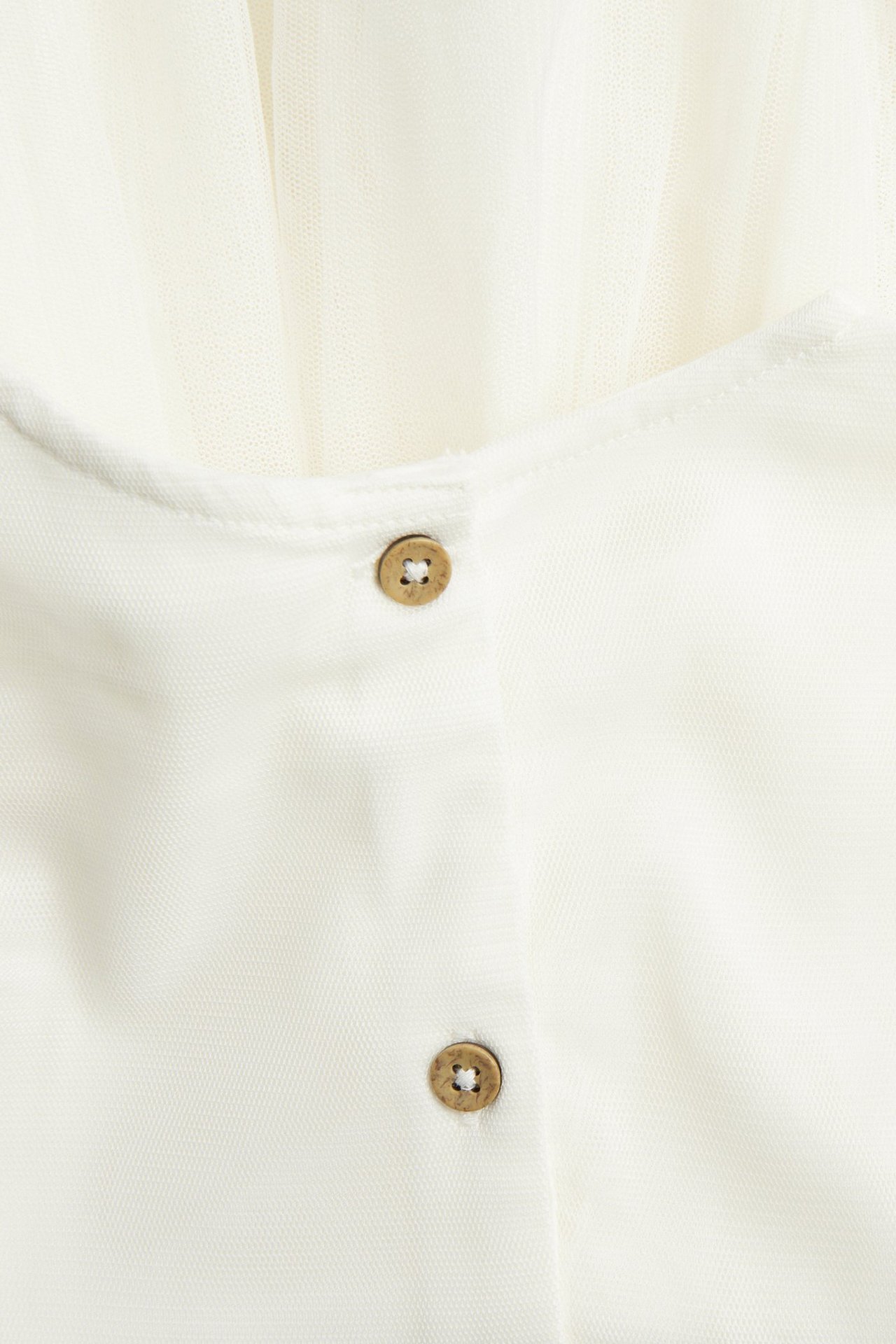 Zbliżenie na kremową sukienkę z siateczki z dwoma brązowymi guzikami na podszewce.