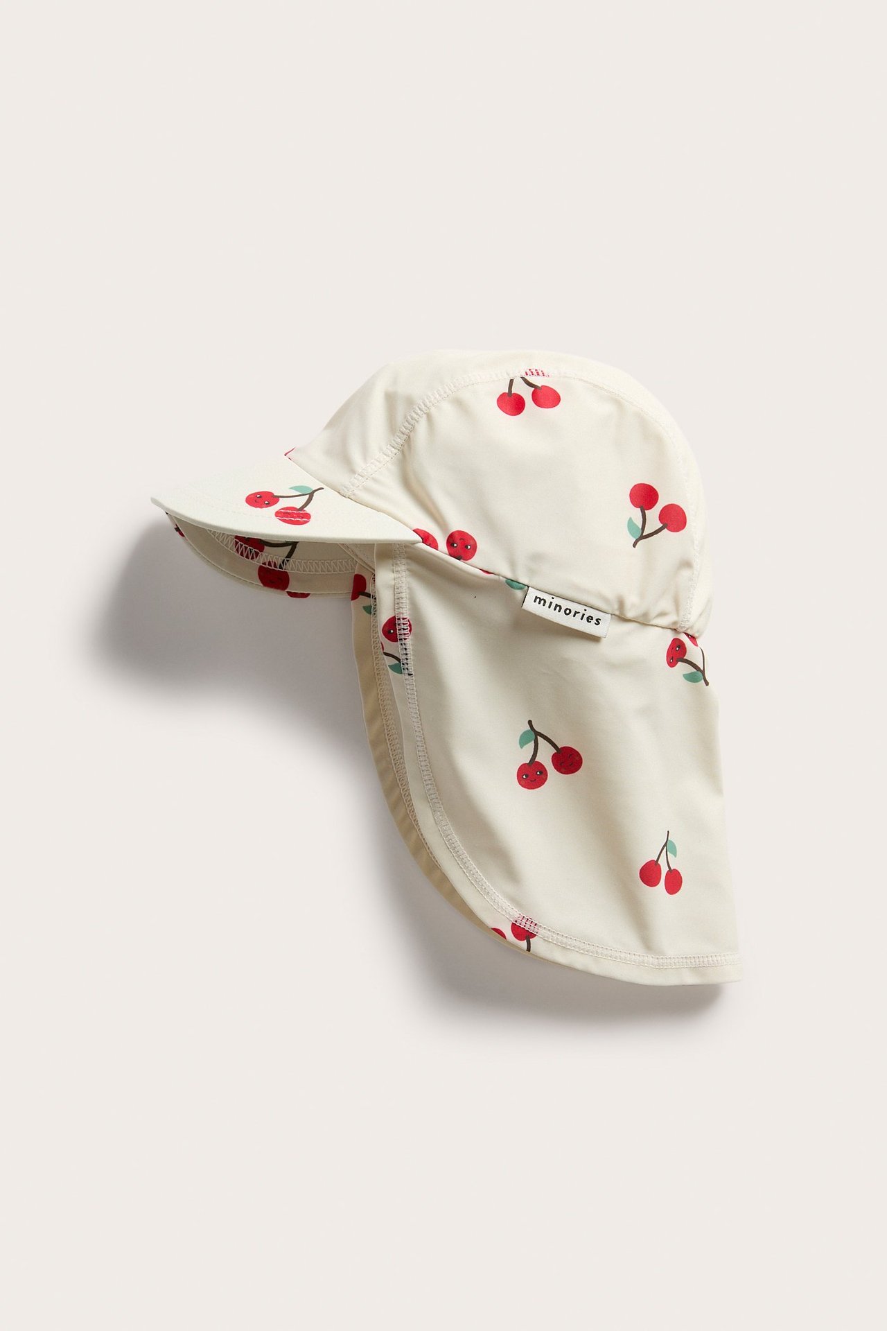 Frontvy av en ljusbeige UV-keps för barn med körsbärsmönster och nackskydd.