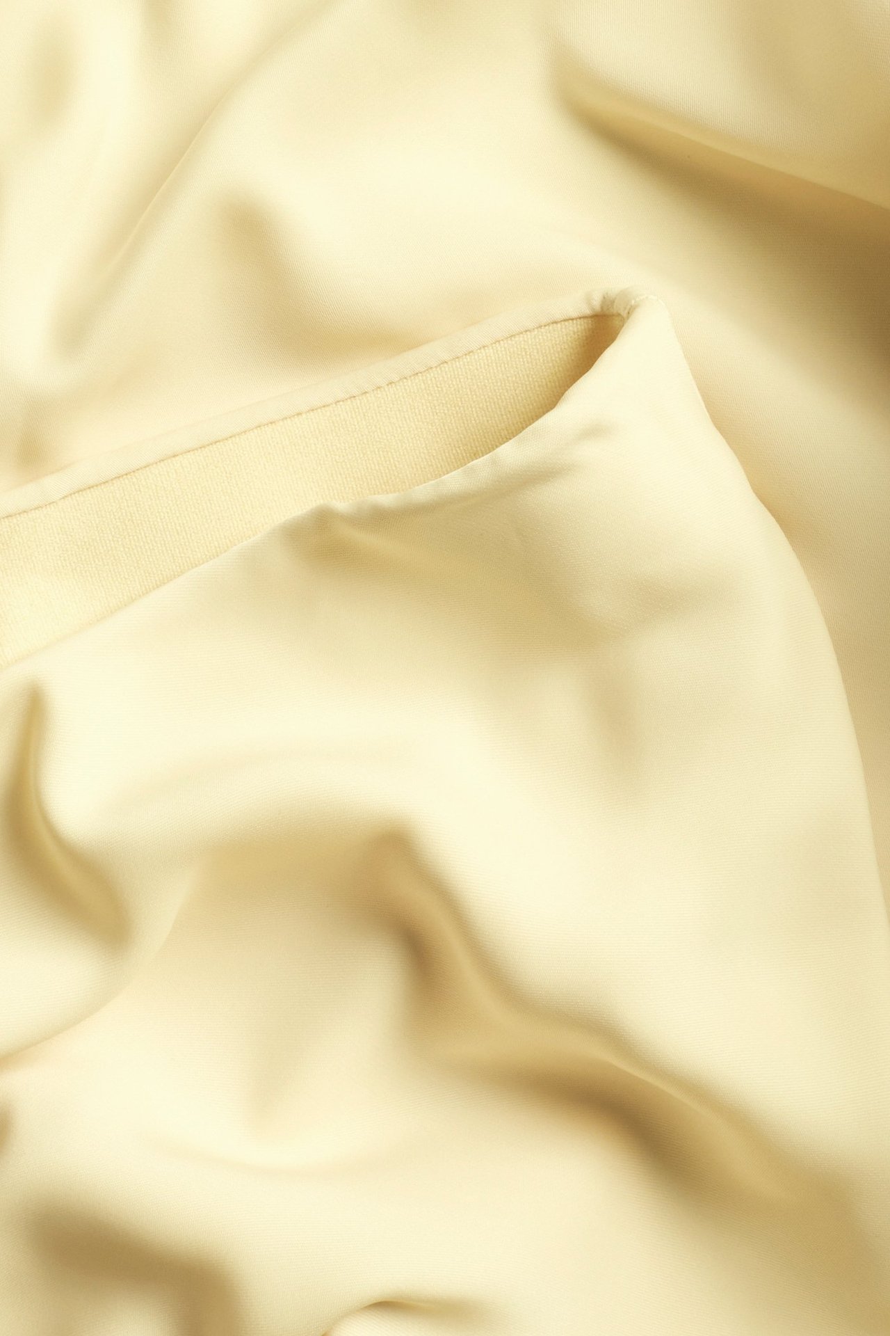 Zbliżenie żółtego, błyszczącego materiału satynowej spódnicy z widocznym szwem.