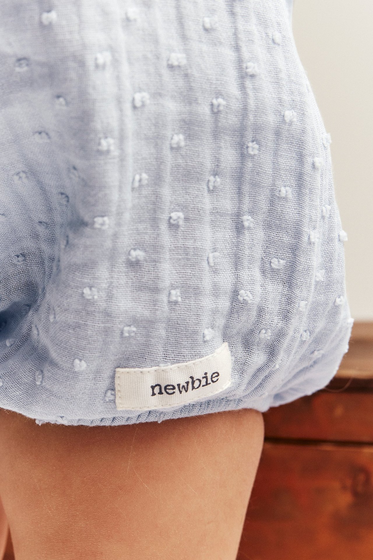 Närbild på bebisben i en ljusblå mönstrad bomulls-playsuit med en vit tygetikett.