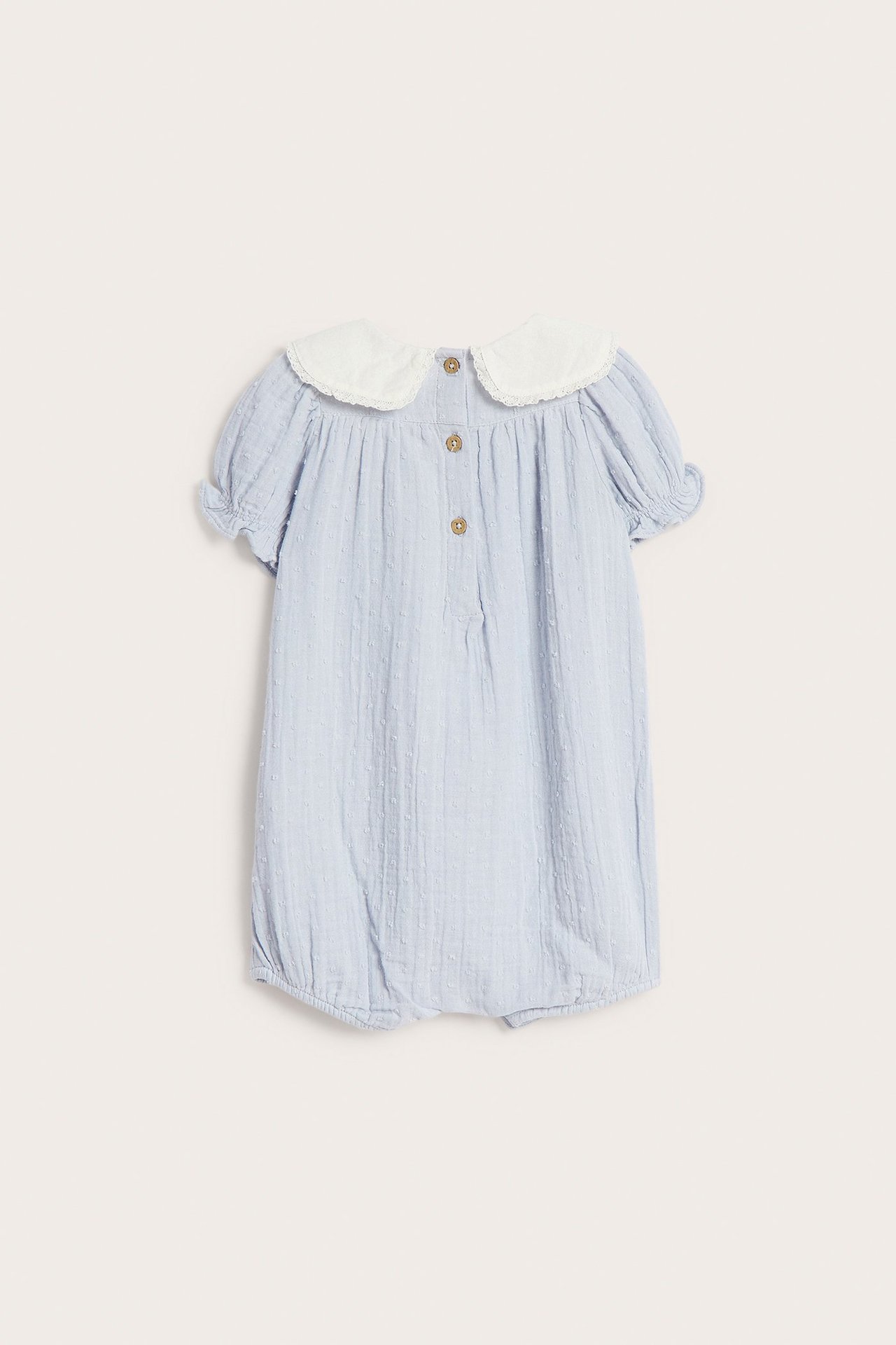Framifrån, ljusblå babyplaysuit med diskret prickstruktur, korta ärmar, vit sjömanskrage och knappar i ryggen.