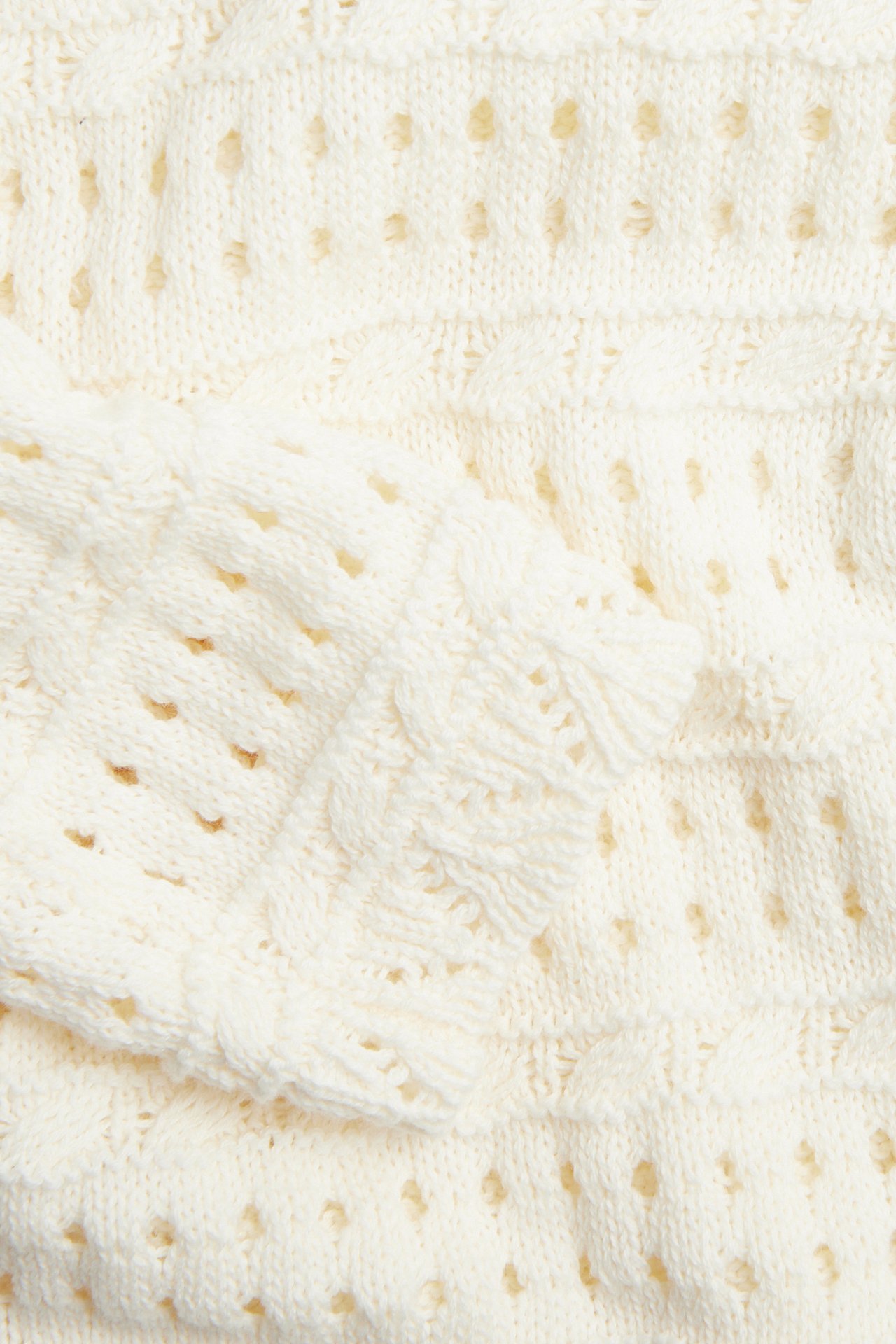 Nærbilde av en off-white, hullstrikket bomullsgenser med flettestrikkede detaljer på ermet.