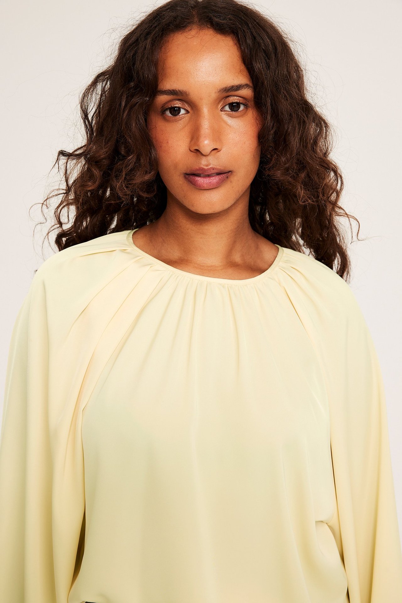 Zbliżenie na kobietę w luźnej, jednolitej żółtej bluzce z marszczonym dekoltem i obszernymi rękawami.