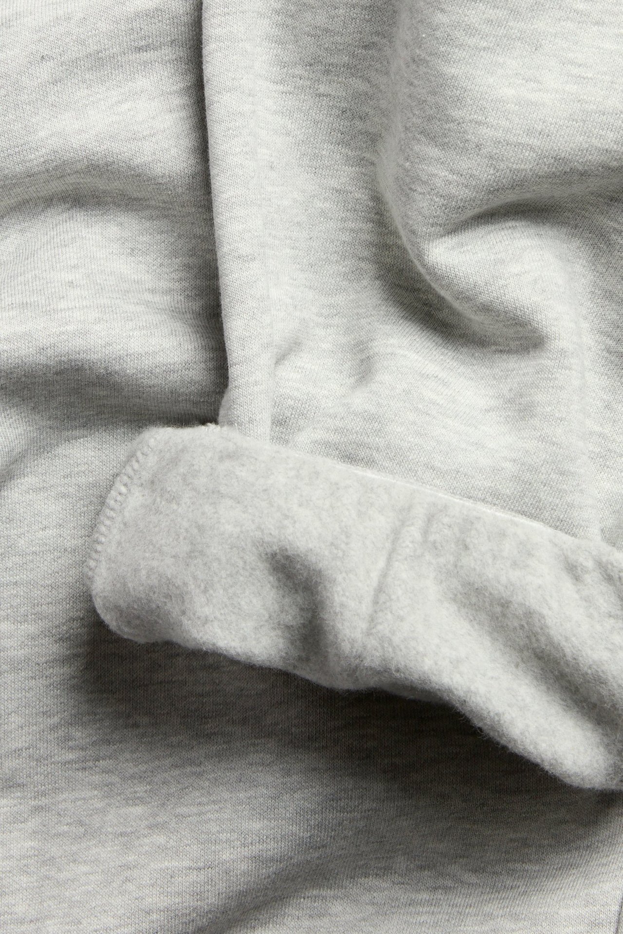 Lähikuva meleeratusta vaaleanharmaasta collegekankaasta, jossa näkyy taitetun reunan pehmeä harjattu sisäpuoli.