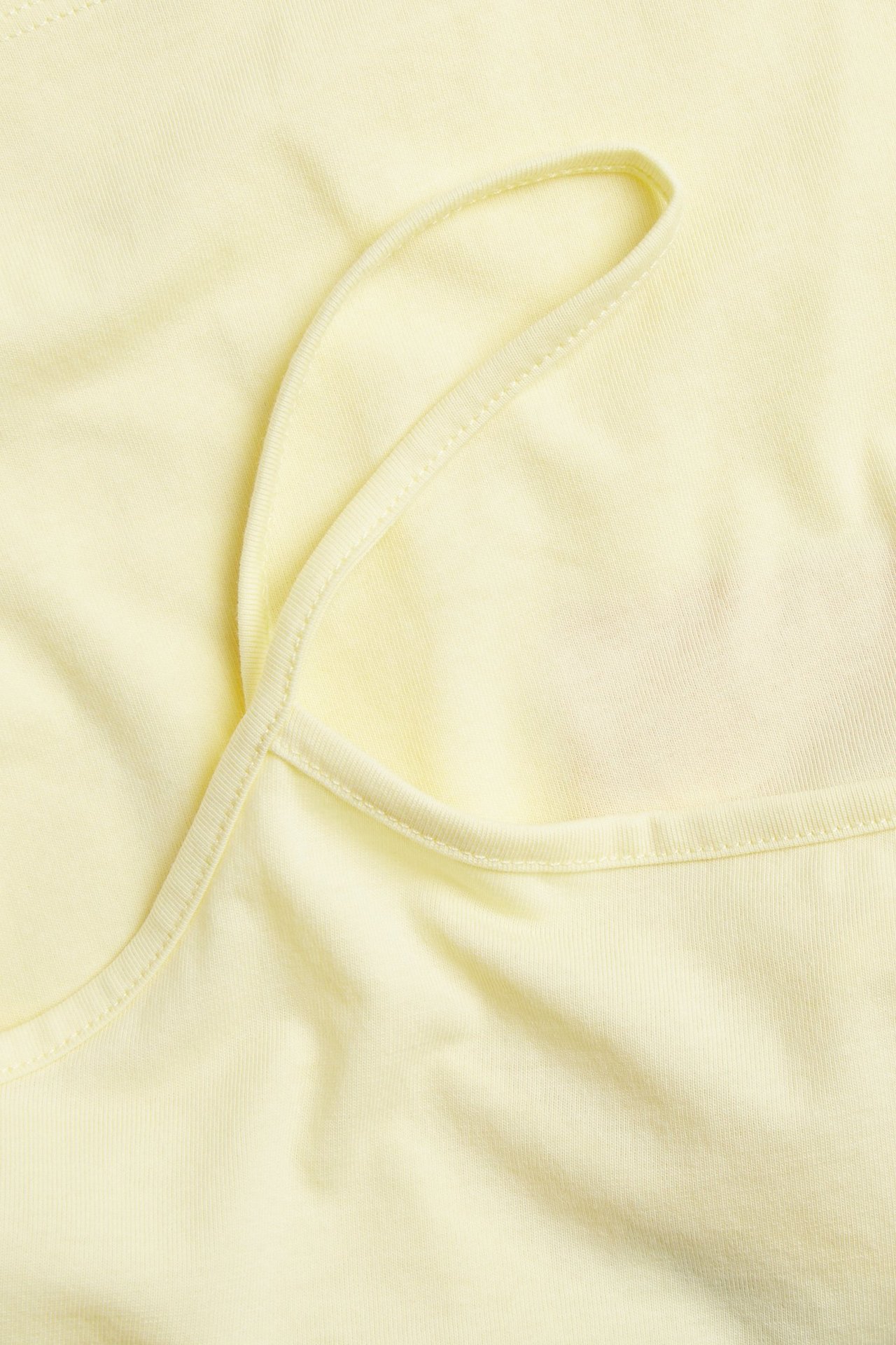 Närbild, uppifrån, av ett ljusgult enfärgat linne med smala axelband.