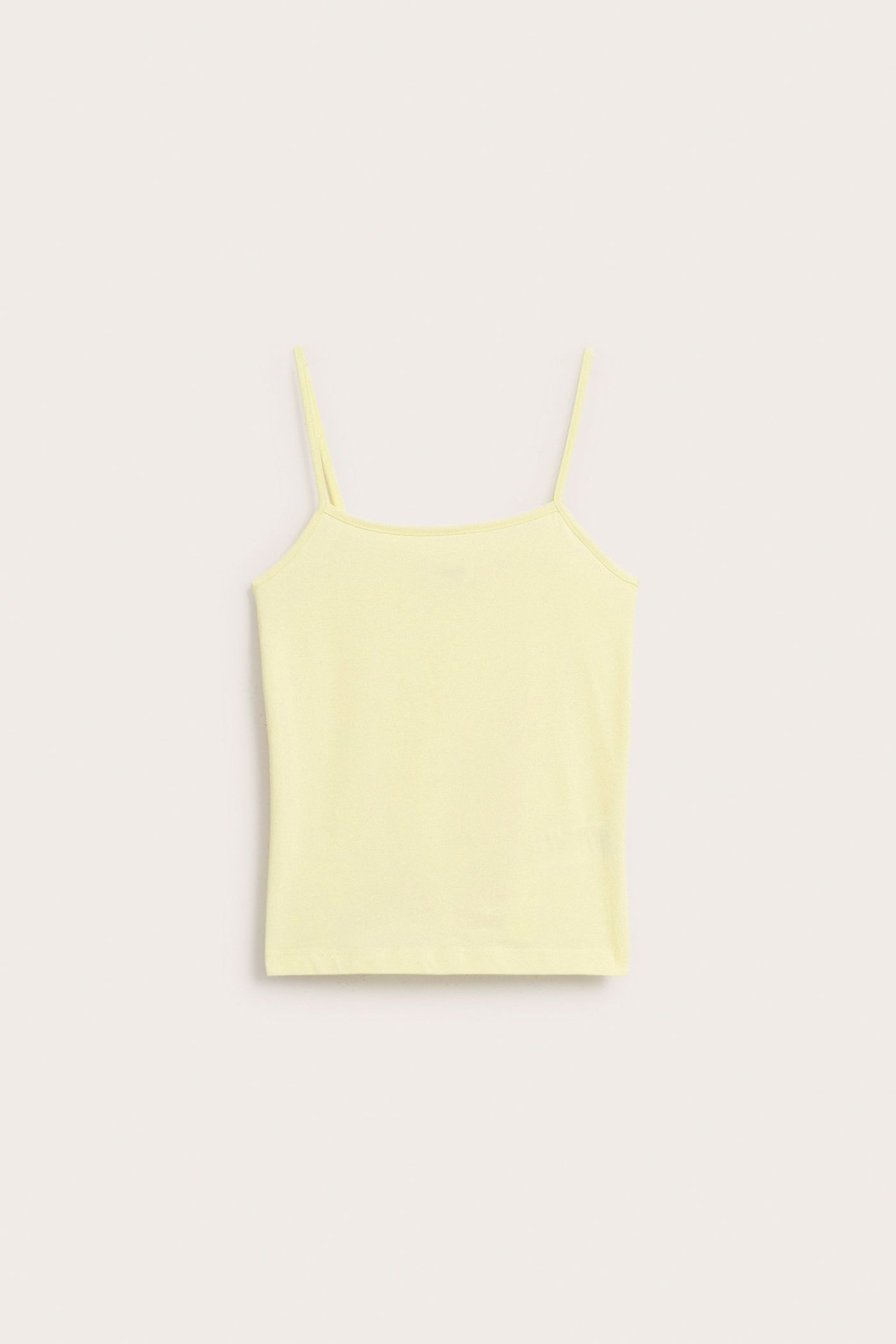 Widok z przodu na jasnożółty, jednolity top dziecięcy z cienkimi ramiączkami.