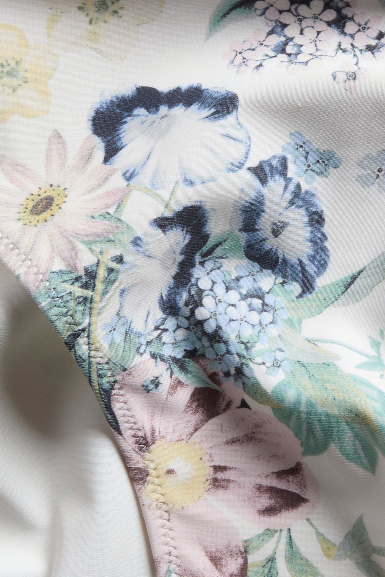 Närbild av en offwhite mönstrad bikinitrosa med blå, rosa och gula blommönster.