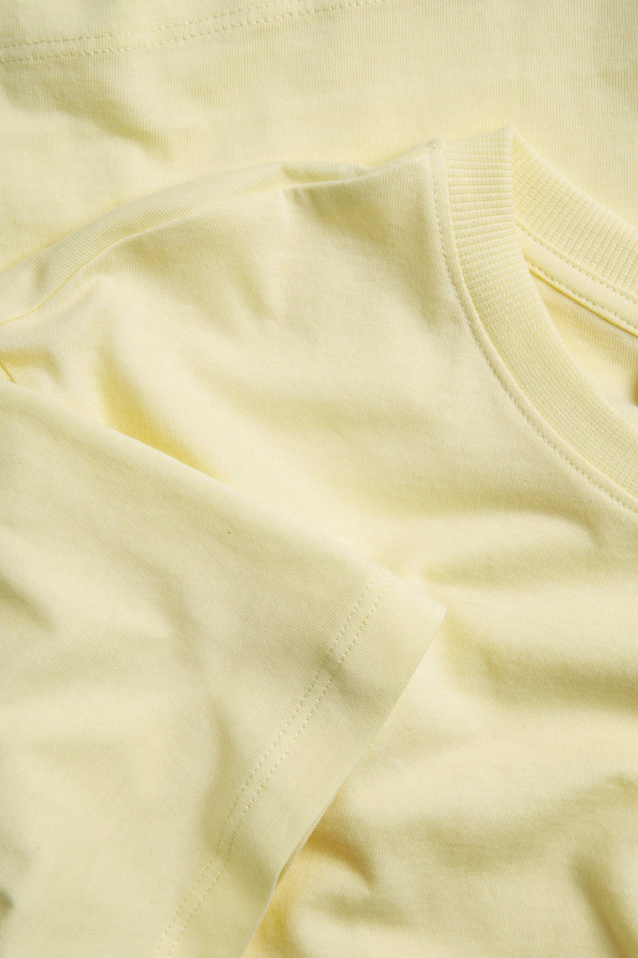 Zbliżenie złożonej, jasnożółtej bawełnianej koszulki z prążkowanym okrągłym dekoltem i krótkimi rękawami.