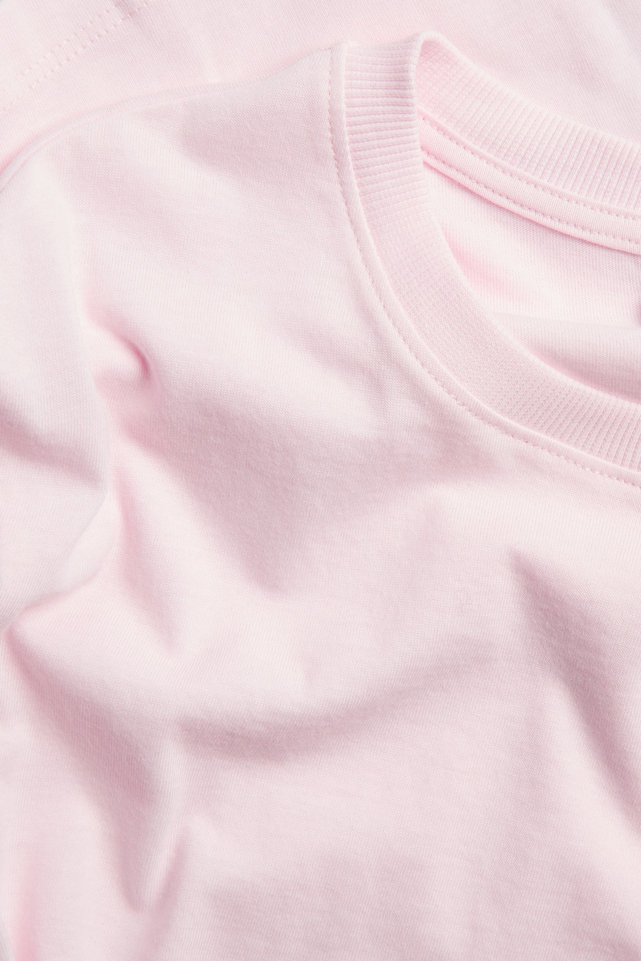 Zbliżenie jasnoróżowej, gładkiej koszulki bawełnianej z prążkowanym okrągłym dekoltem.