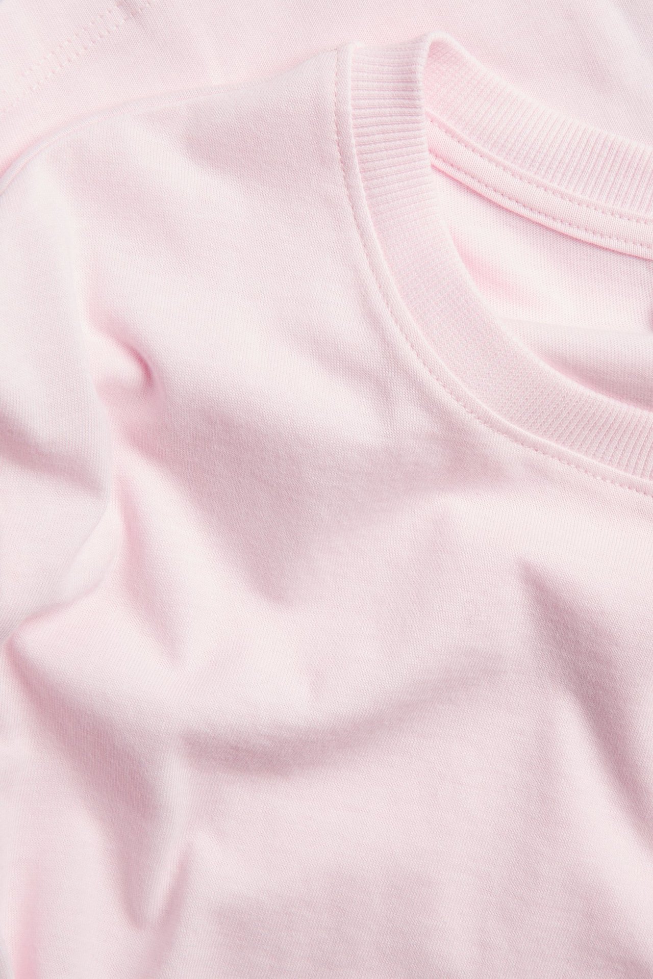 Zbliżenie jasnoróżowej, gładkiej koszulki bawełnianej z prążkowanym okrągłym dekoltem.