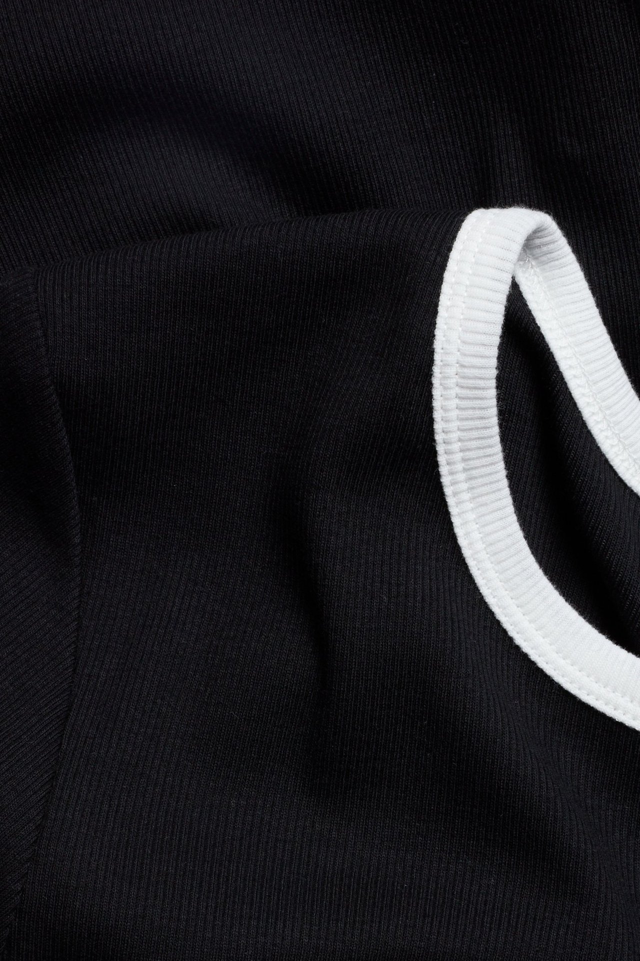 Zbliżenie czarnego prążkowanego baby tee z białymi kontrastowymi lamówkami.