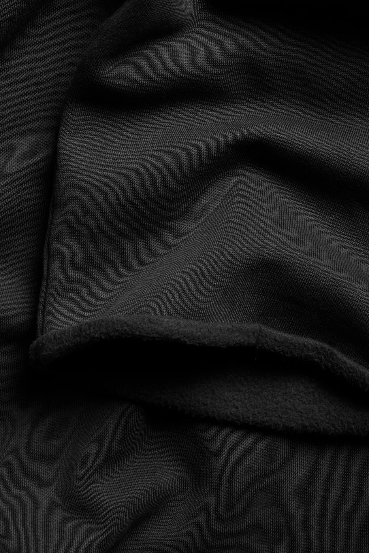 Nærbilde av svart joggebukse-stoff, som viser den glatte jersey-yttersiden og myk, børstet fleece-innsiden.