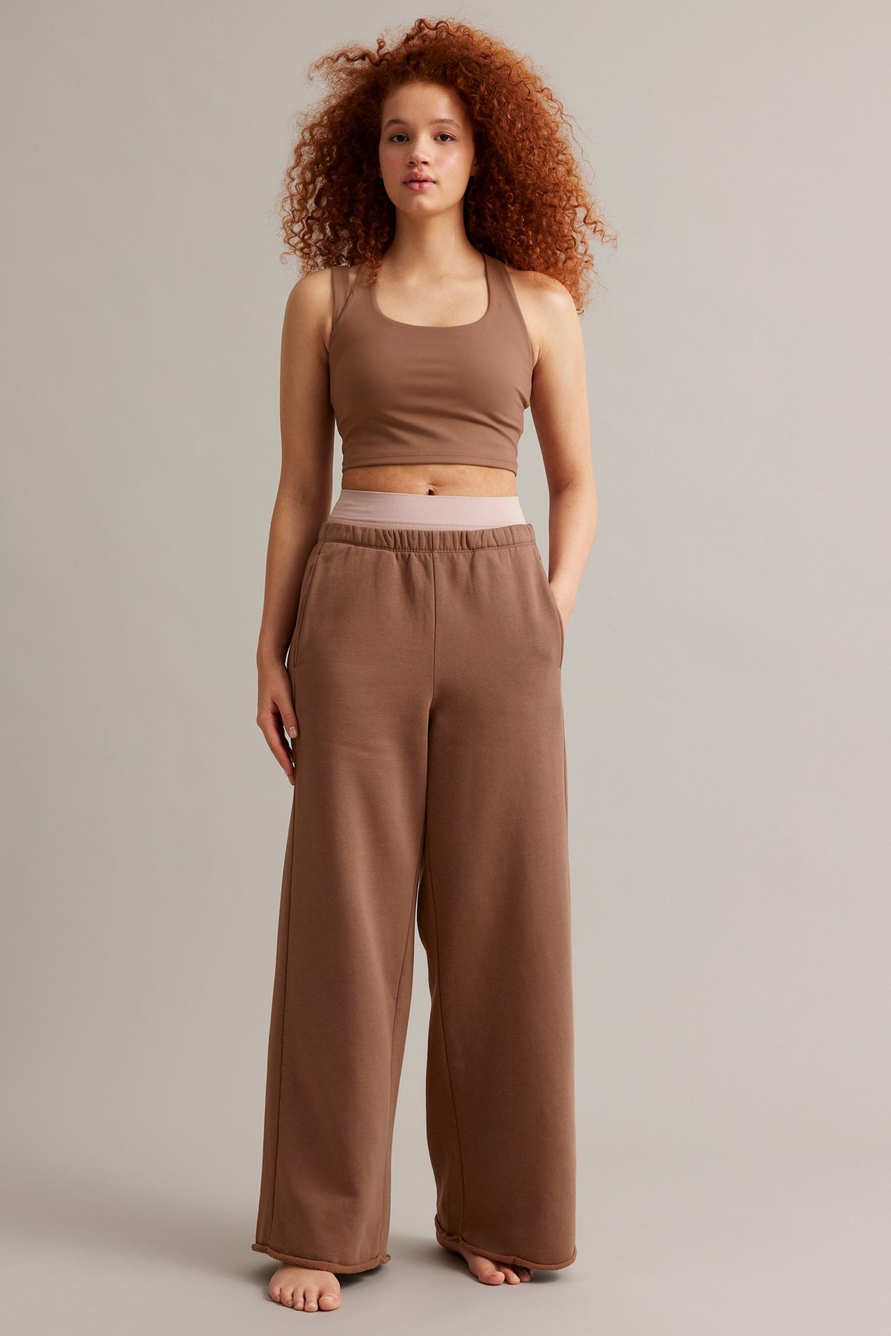 Etunäkymä: Nainen ruskeissa leveälahkeisissa collegehousuissa joustovyötäröllä ja yhteensopivassa ruskeassa crop topissa.