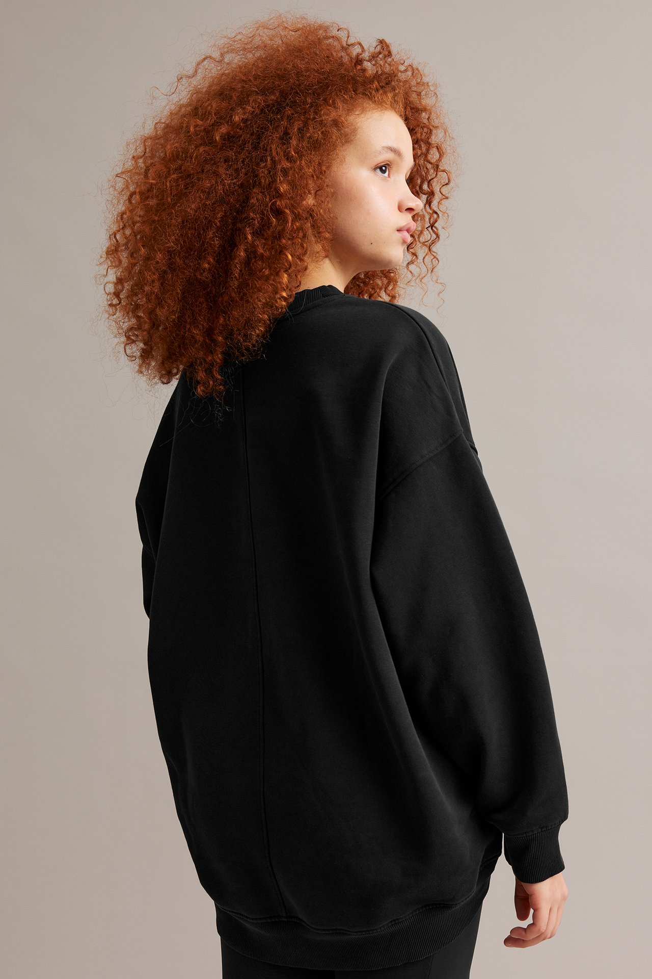 Sidovy bakifrån av ett barn i en oversize svart lång sweatshirt med tvättad look och ribbade muddar.