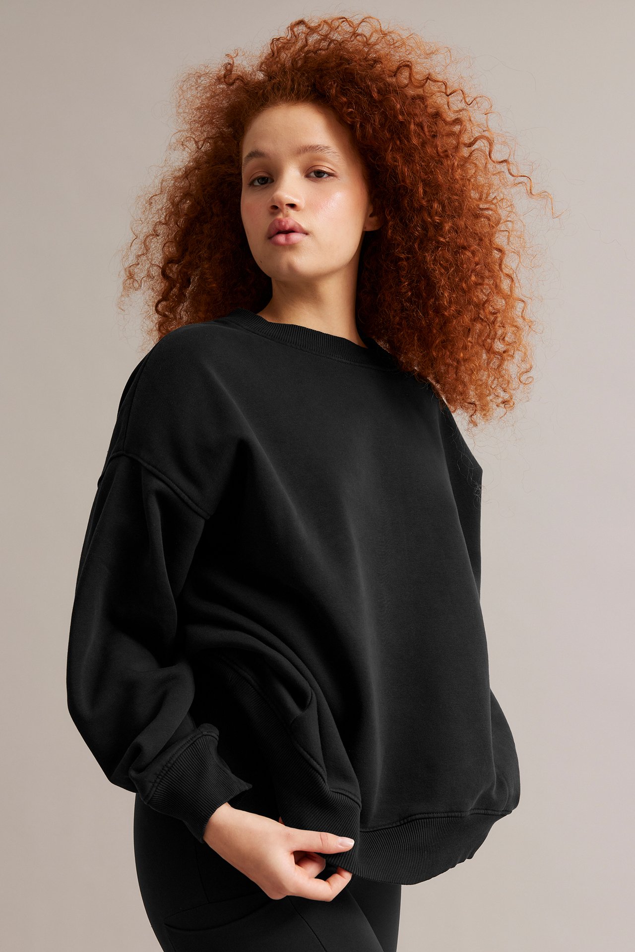 Framifrån: Kvinna i lång svart sweatshirt med tvättad look och oversized passform, över svarta leggings.
