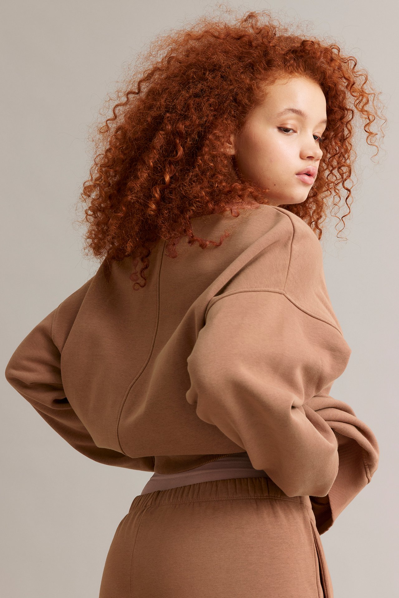 Ryggvy av en kvinna i en lång brun sweatshirt med synliga sömmar och matchande sweatpants.