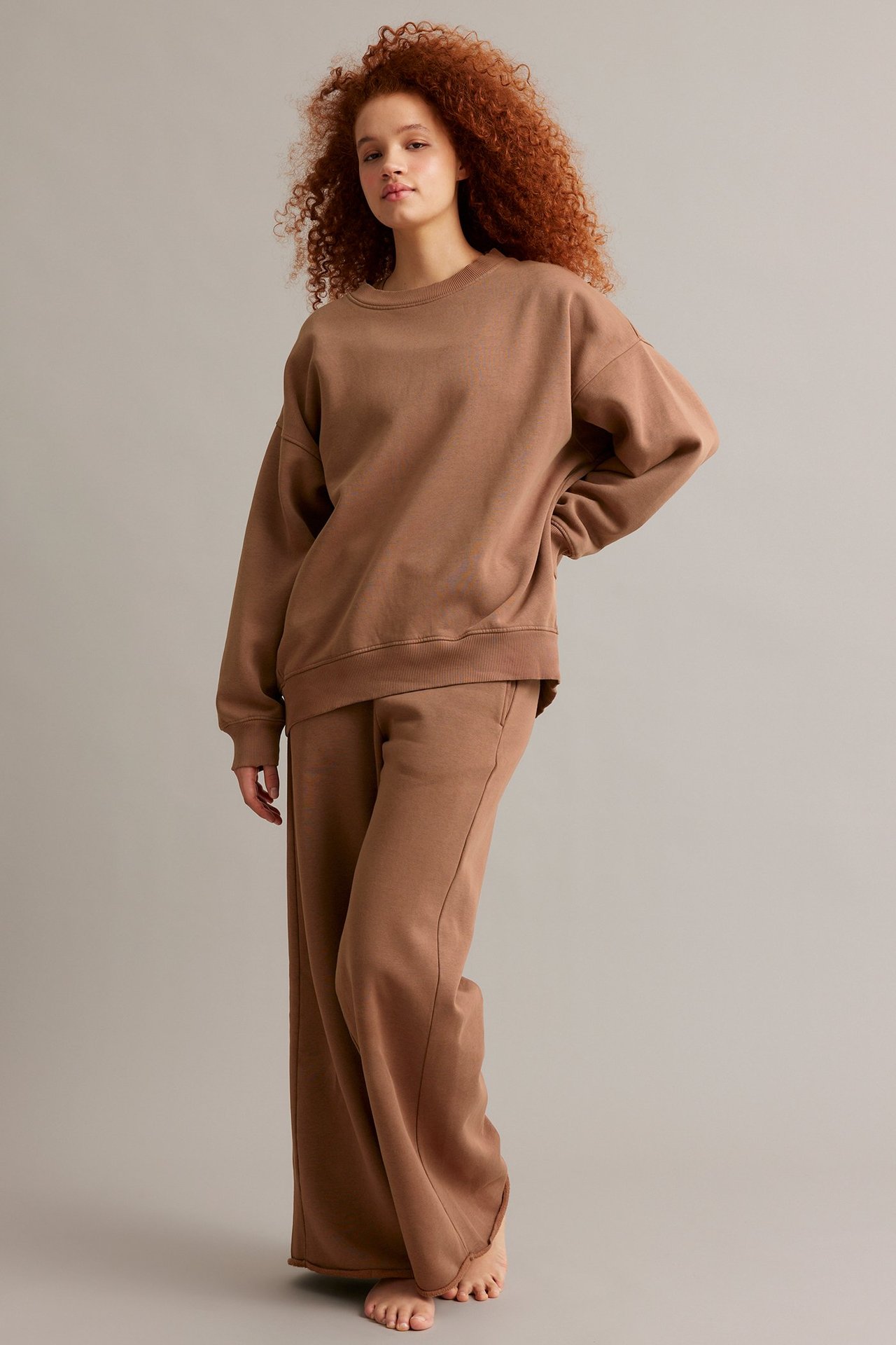 Nainen edestäpäin yllään ylisuuri ruskea pitkä collegepaita ja yhteensopivat leveälahkeiset collegehousut.