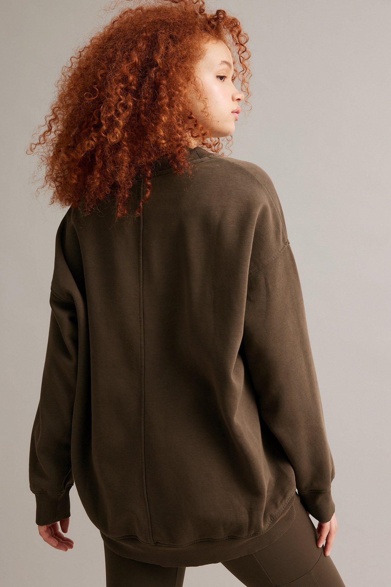 Widok z tyłu i boku kobiety w długiej, brązowej spranej bluzie i pasujących brązowych spodniach.