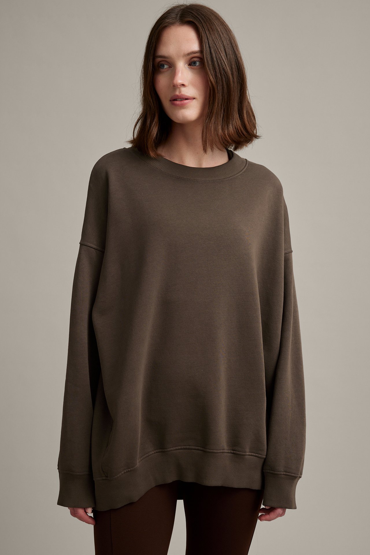 Frontvisning: Kvinne i mørkebrun oversized sweatshirt med vasket utseende og mørkebrun bukse.