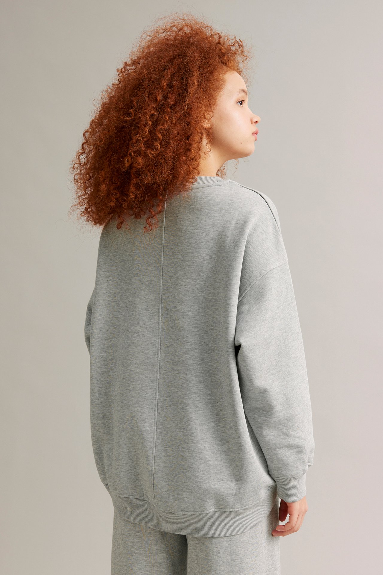 Ryggvy av en kvinna i en ljusgråmelerad oversized lång sweatshirt och matchande byxor.